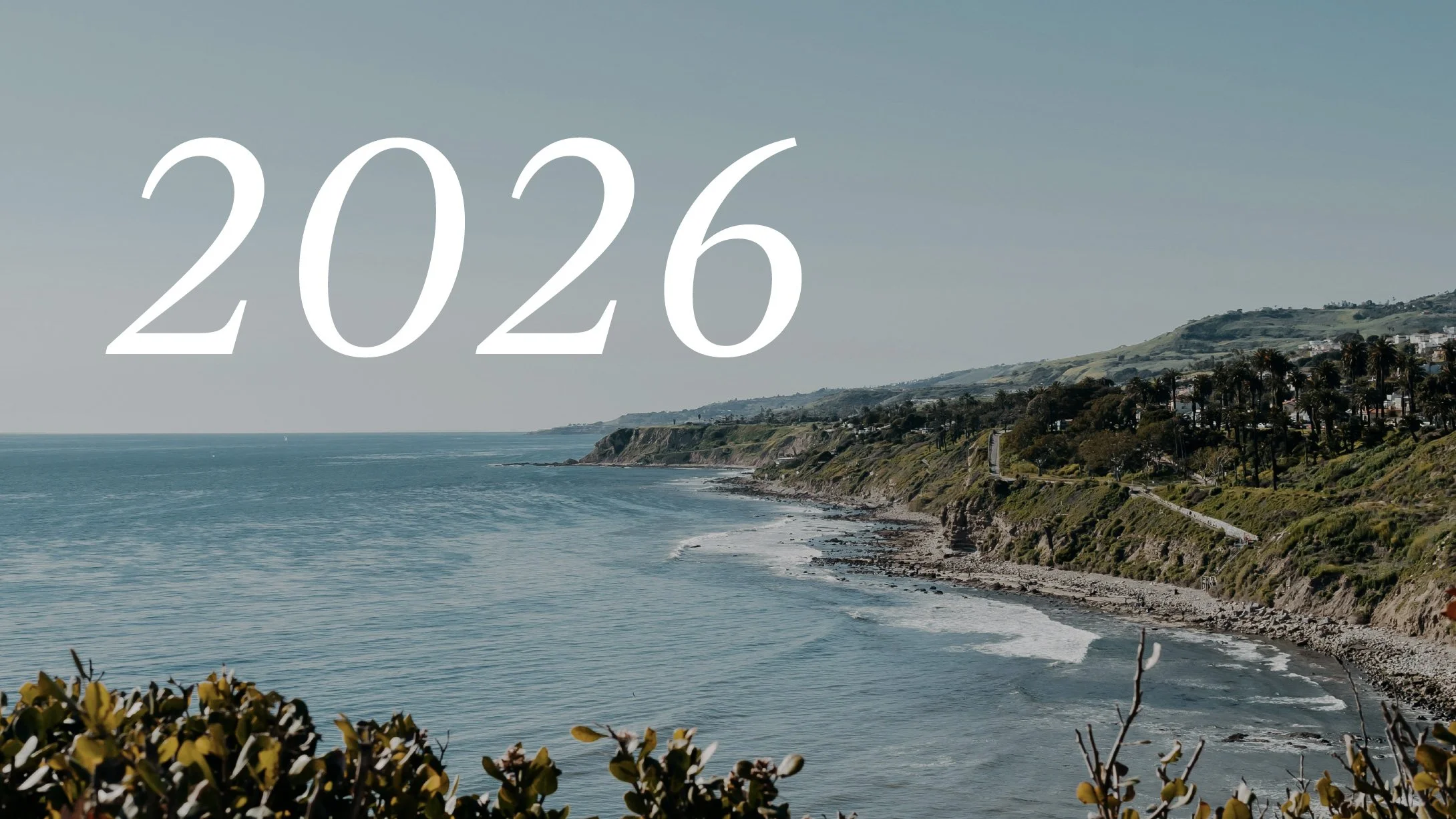 Scenic coastal landscape with ocean, cliffs, and houses on hillside under a clear sky, with the year 2026 overlaid in large white text.