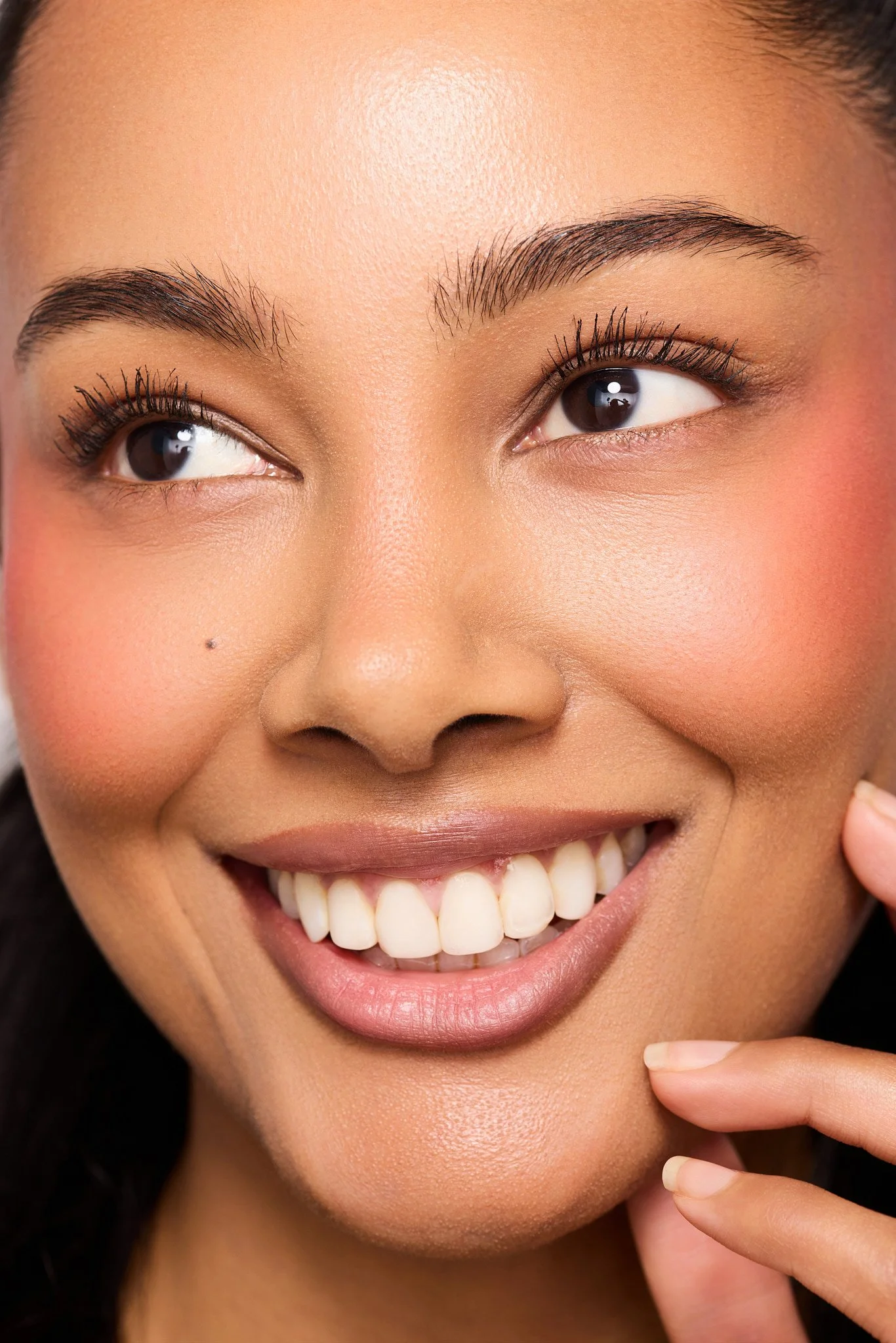 Close-up commercial beauty portrait of model Jennifer Elysee smiling with visible teeth, glowing skin, natural makeup and soft skincare lighting.