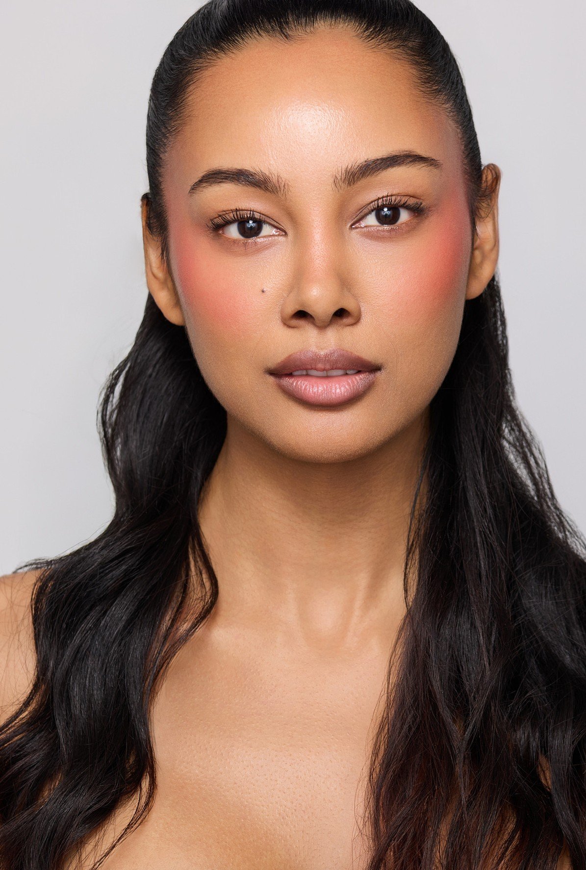 Luxury beauty portrait of commercial model Jennifer Elysee featuring soft pink makeup and long dark wavy hair.