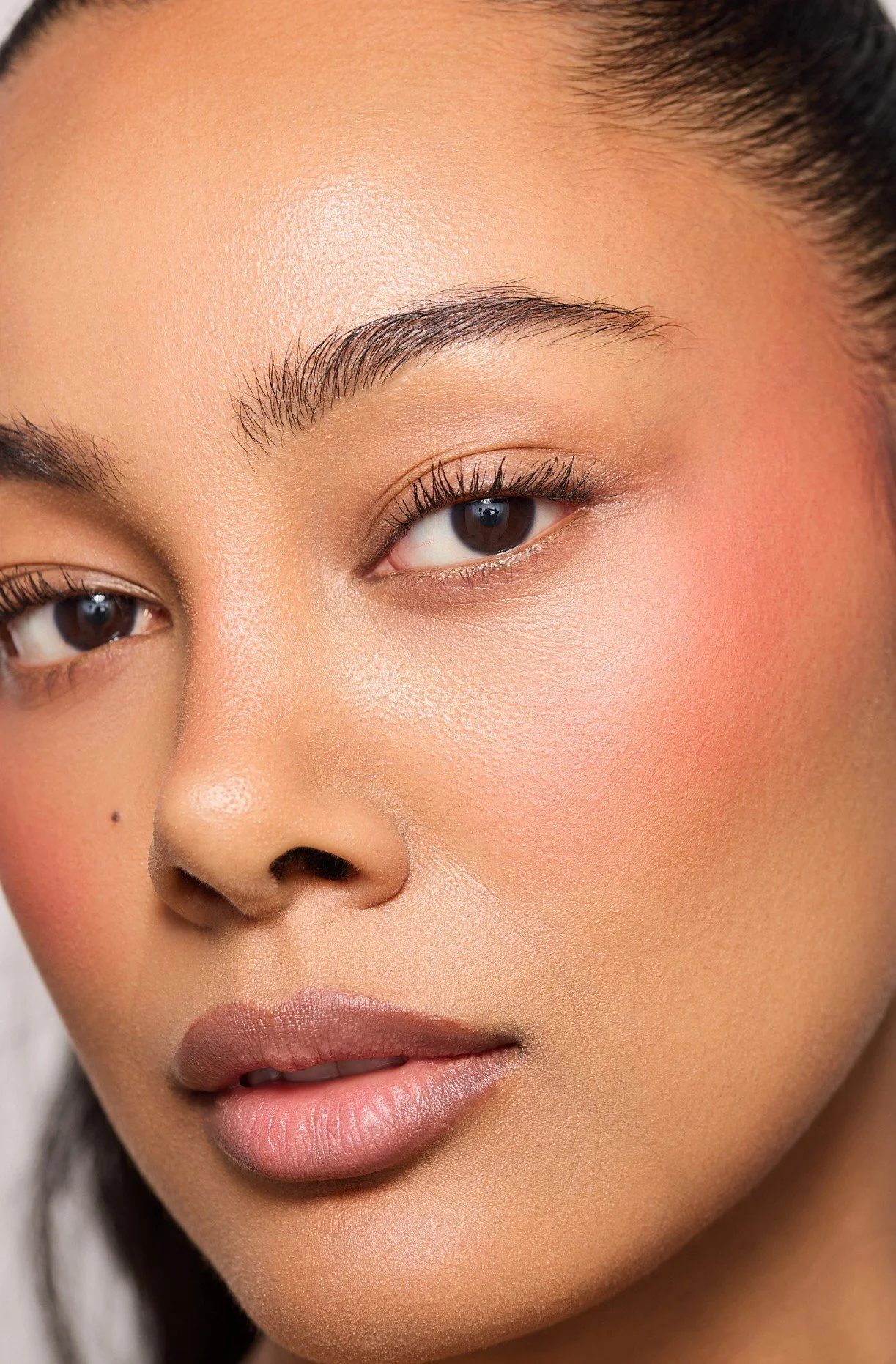 Luxury cosmetics beauty close-up of London model Jennifer Elysee featuring glowing skin, soft blush makeup and natural brows.