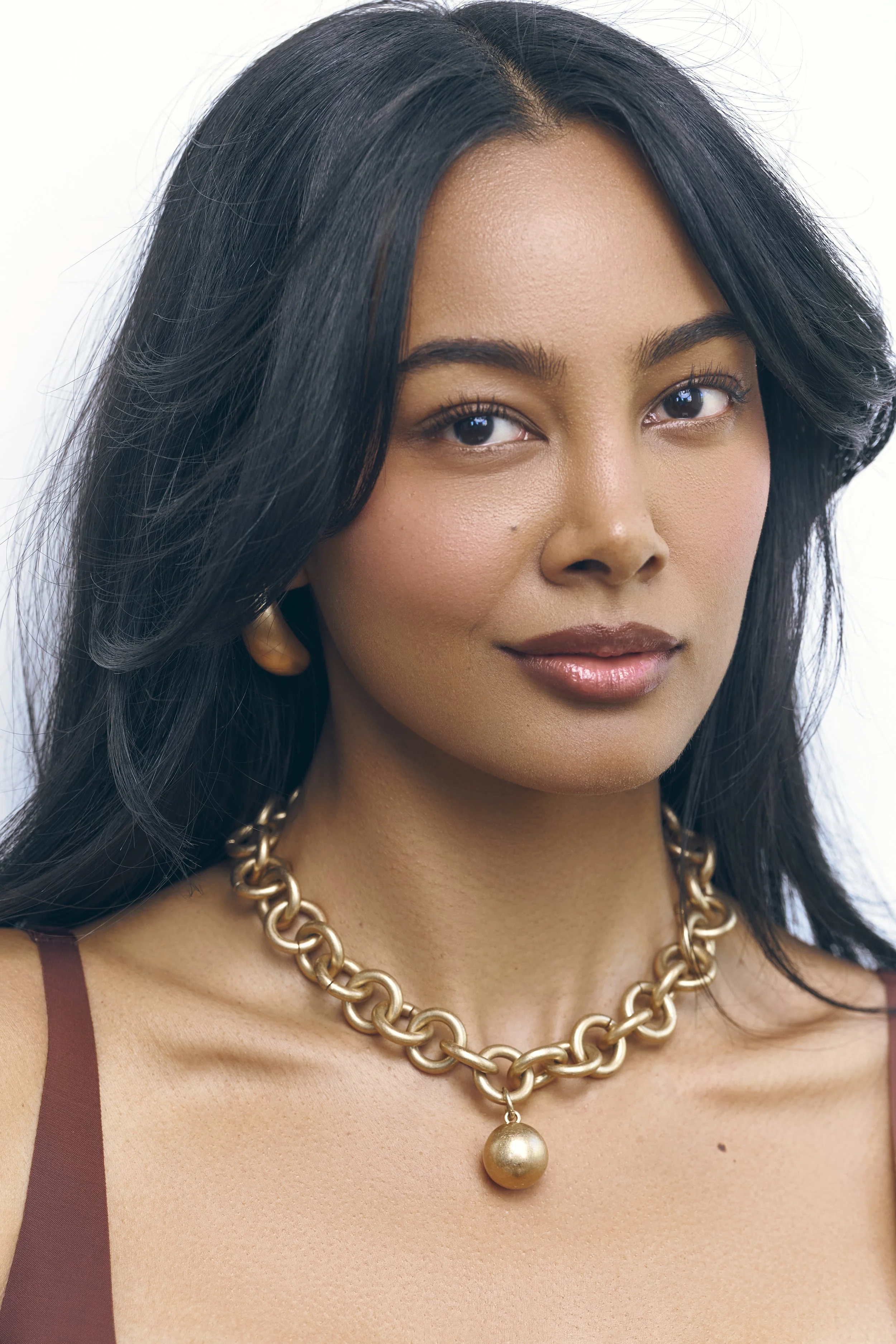 Luxury beauty portrait of Jennifer Elysee with statement gold jewellery, glowing skin and natural makeup.