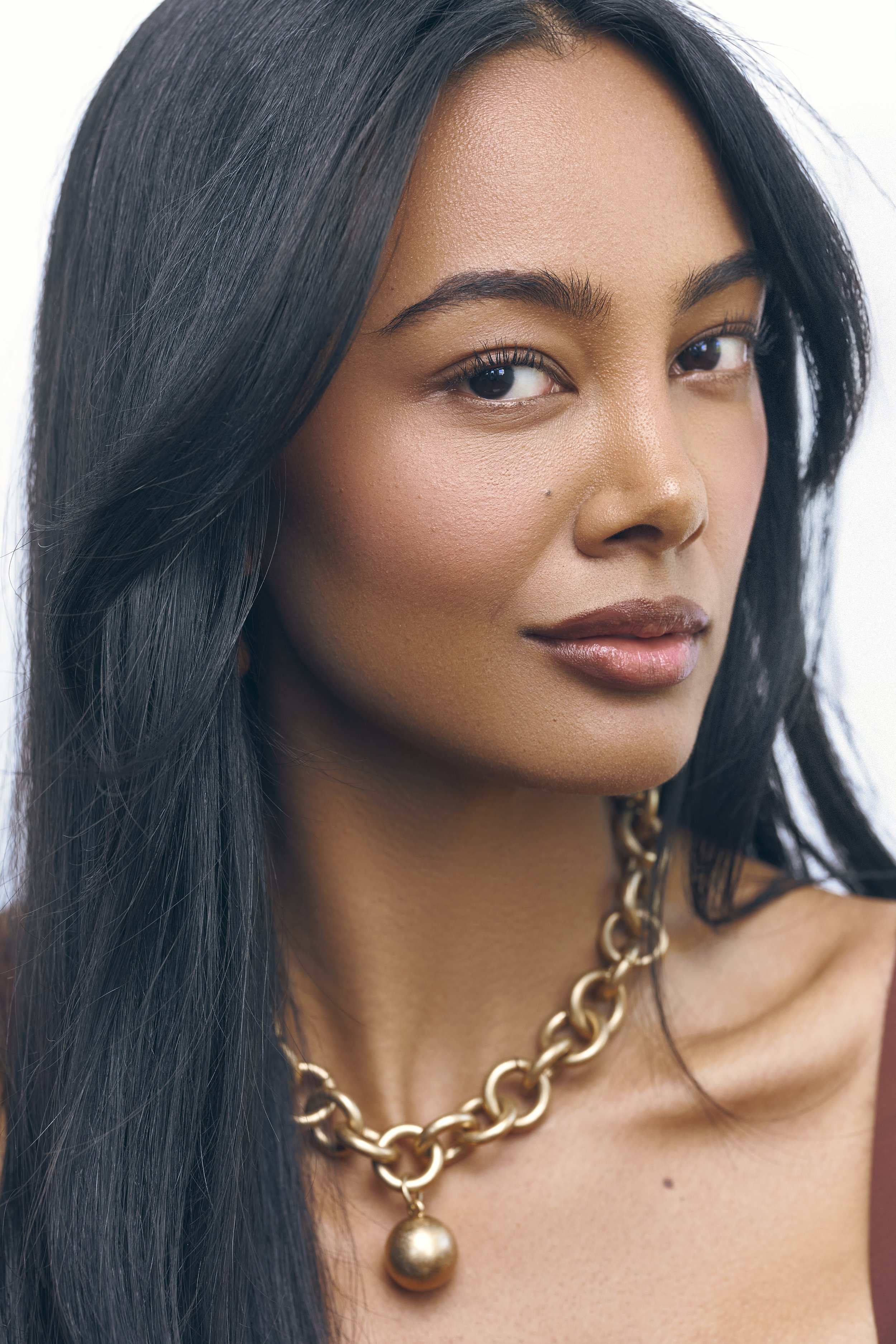 Commercial beauty portrait of London model Jennifer Elysee featuring sleek dark hair, glowing skin and statement gold jewellery.