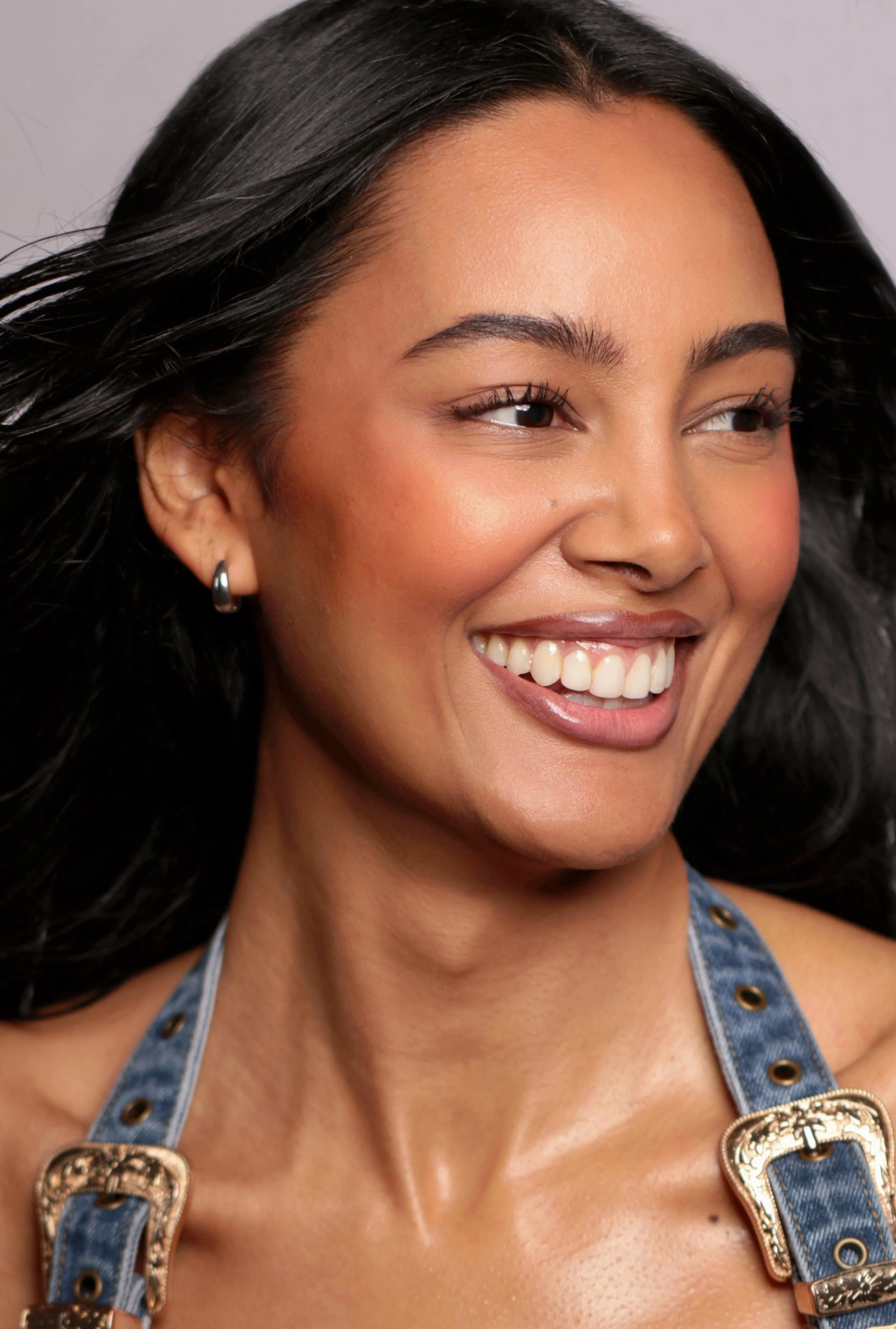 Jennifer Elysee smiling in a warm commercial lifestyle beauty portrait with natural makeup and denim styling.