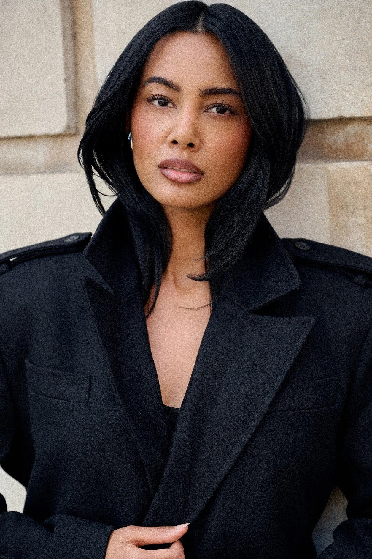 Editorial close-up portrait of Jennifer Elysee in a structured black coat with refined beauty styling and soft natural makeup.
