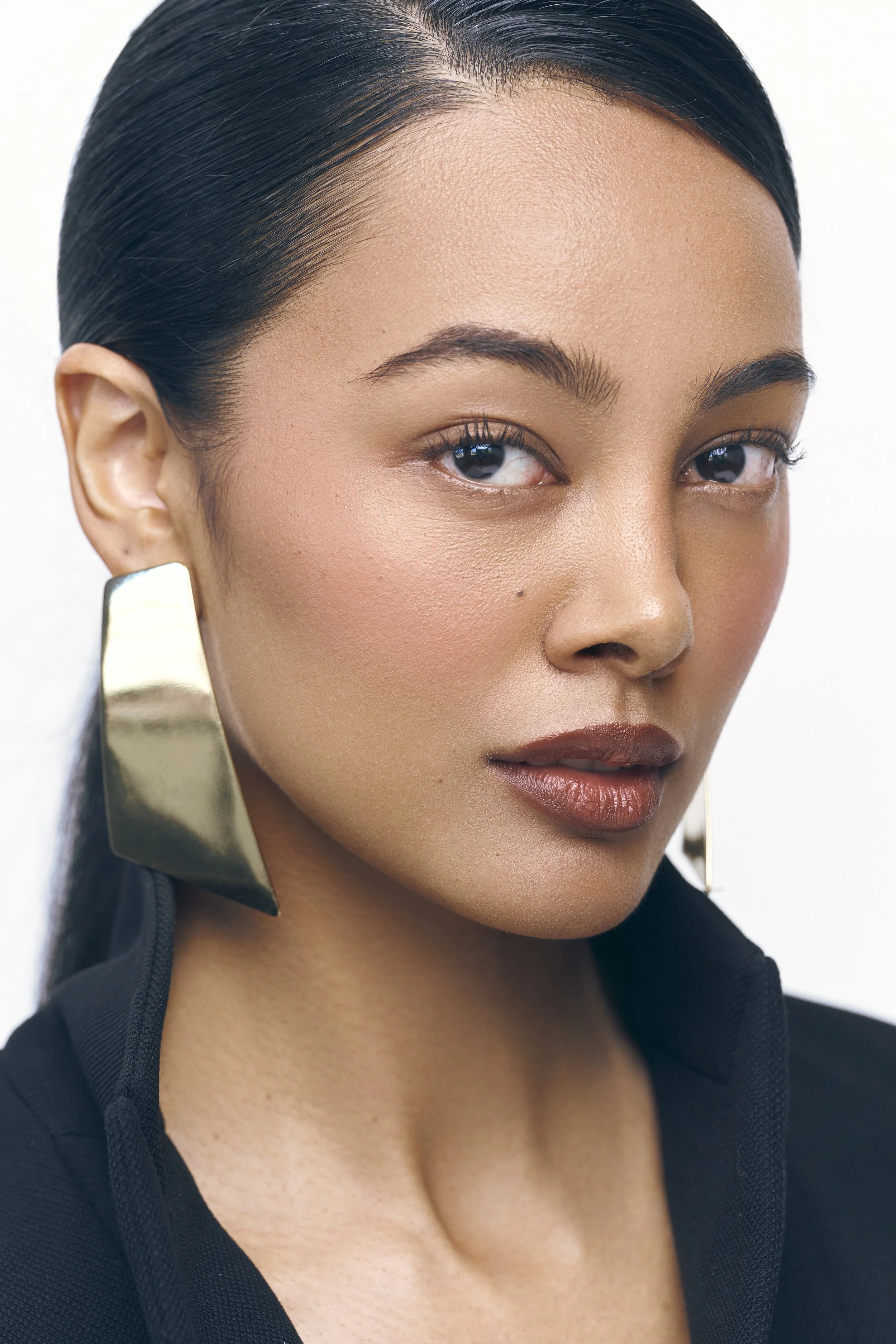 Close-up of a Jennifer Elysee with dark hair, gold statement earrings, and natural makeup