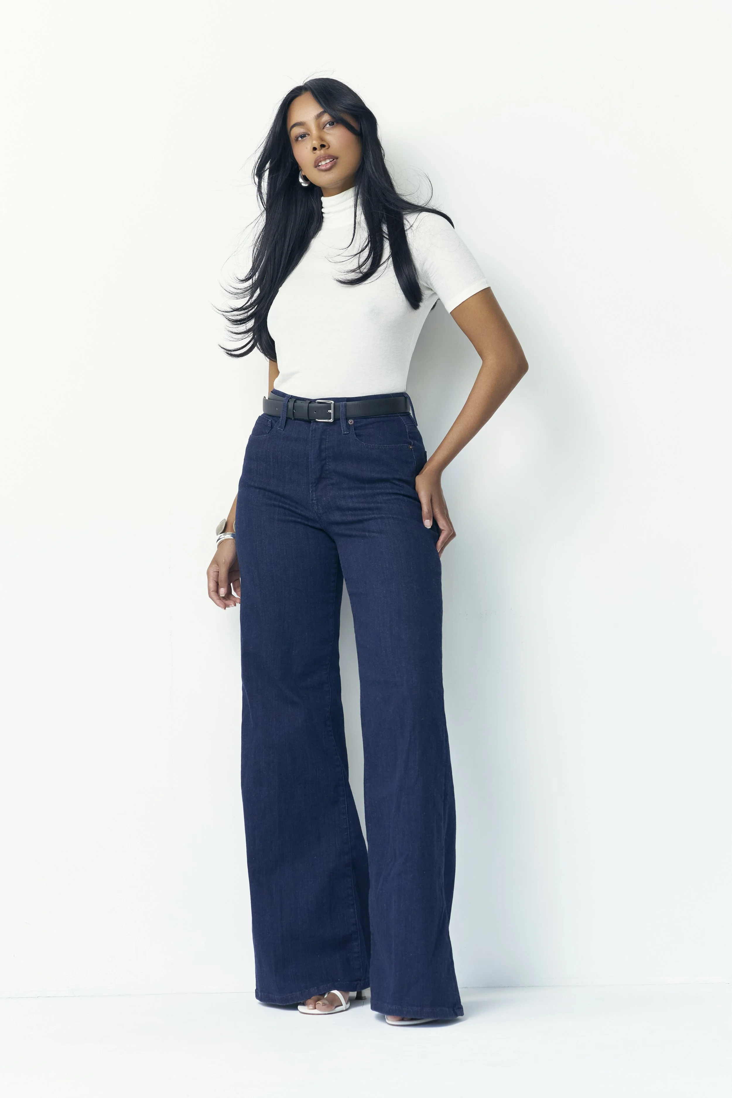 Full-length commercial lifestyle portrait of London model Jennifer Elysée wearing a white high-neck top and dark denim jeans.