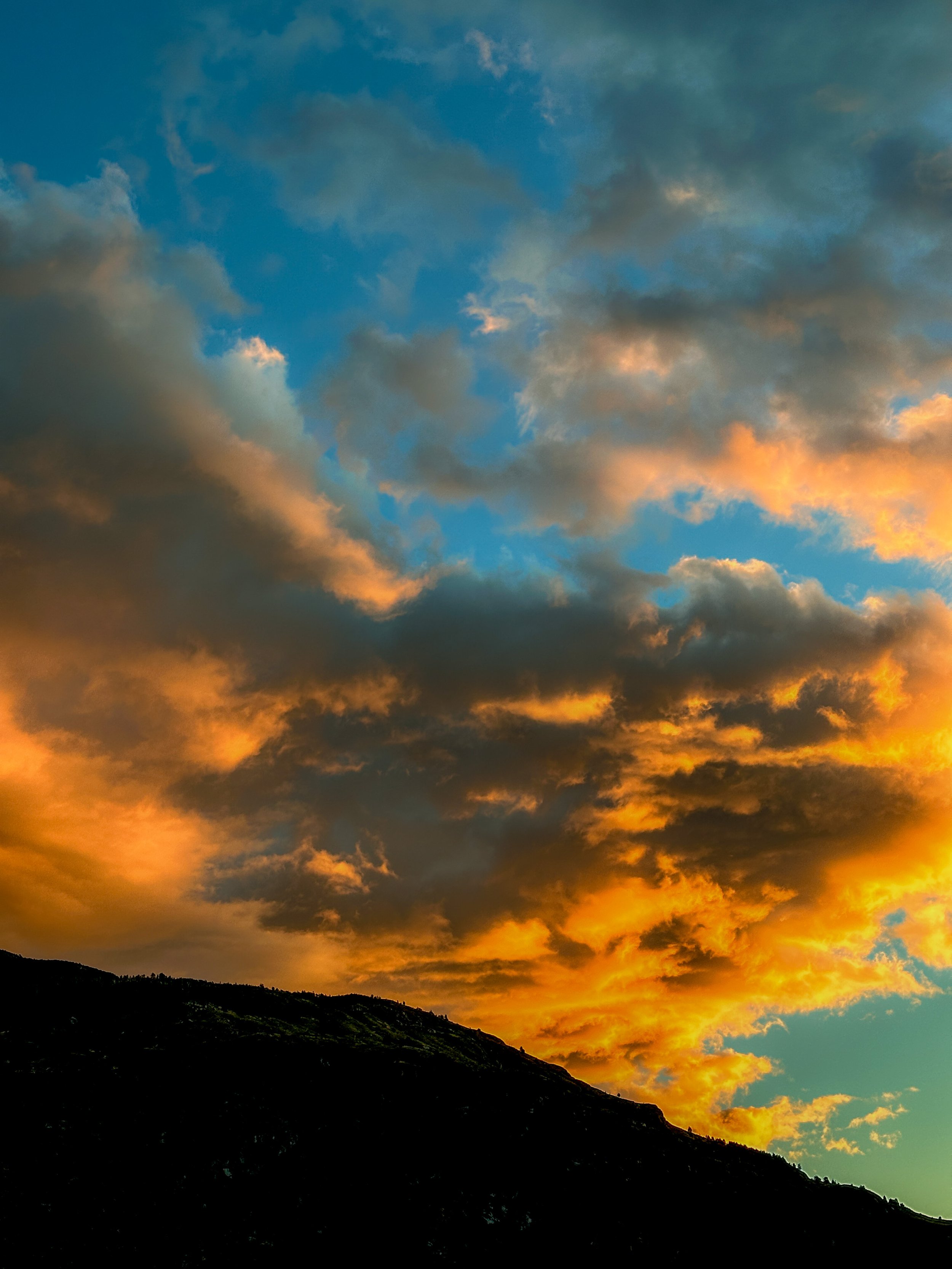 Sunset sky with colorful clouds over a mountain silhouette.