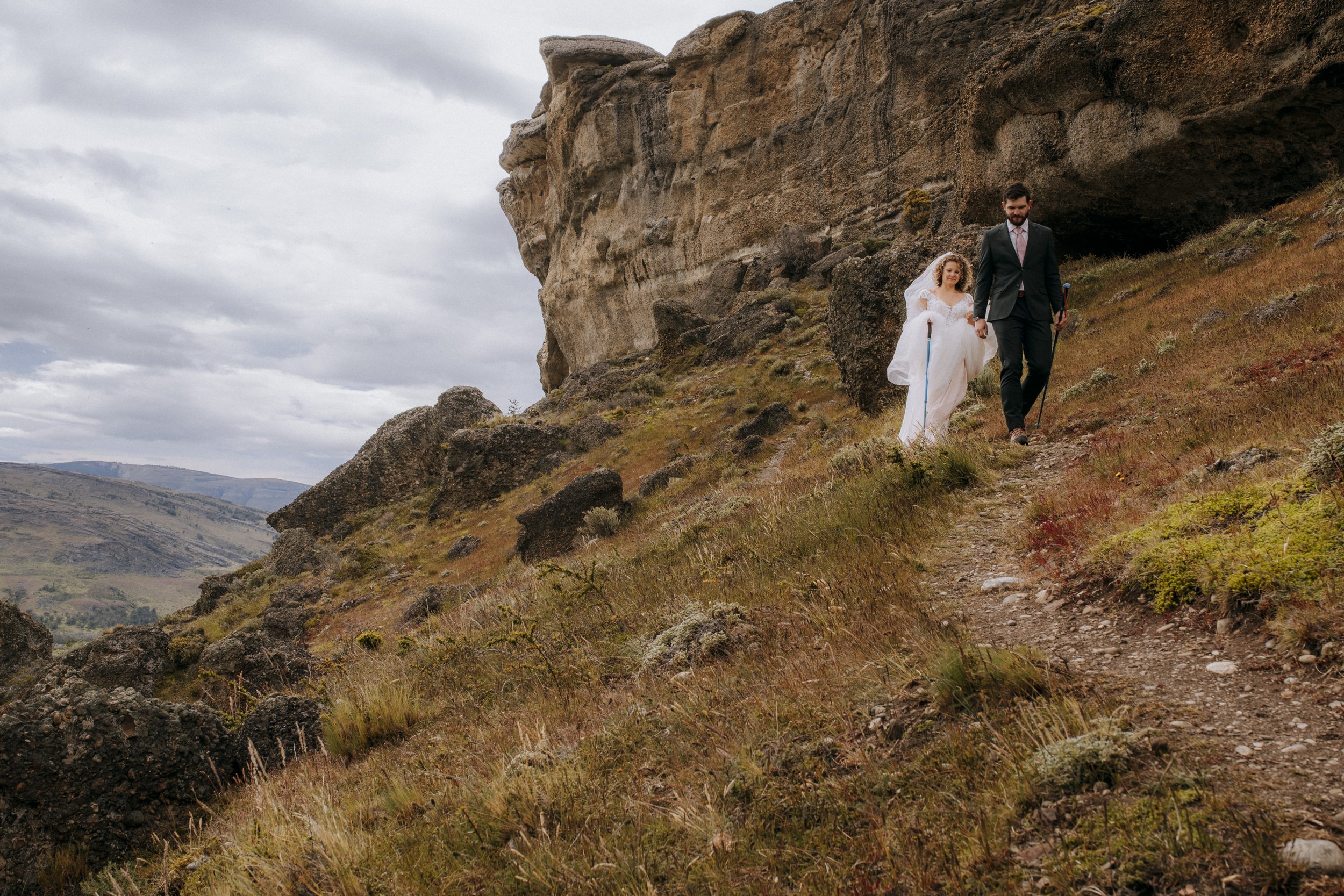 A man and woman in wedding attire walking down through a Patagonia landscape after getting married
