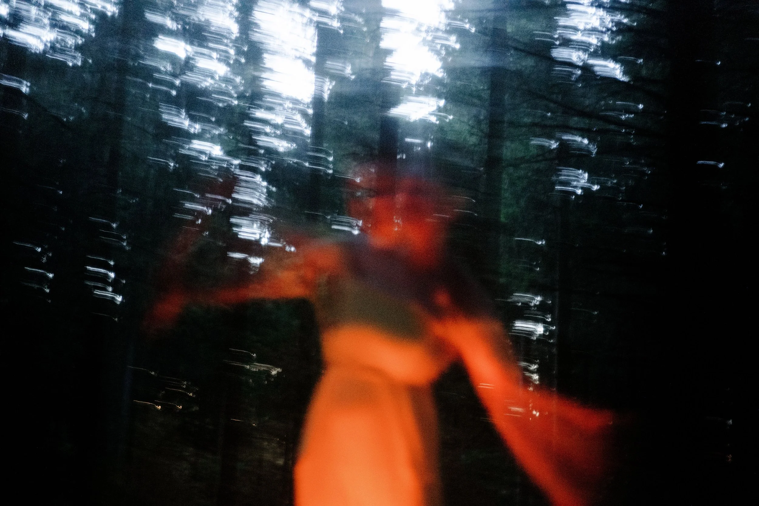 Une image floue montrant des arbres et une lumière rouge-orange au centre, avec des reflets et des bruits visuels à cause du mouvement ou de la faible luminosité.