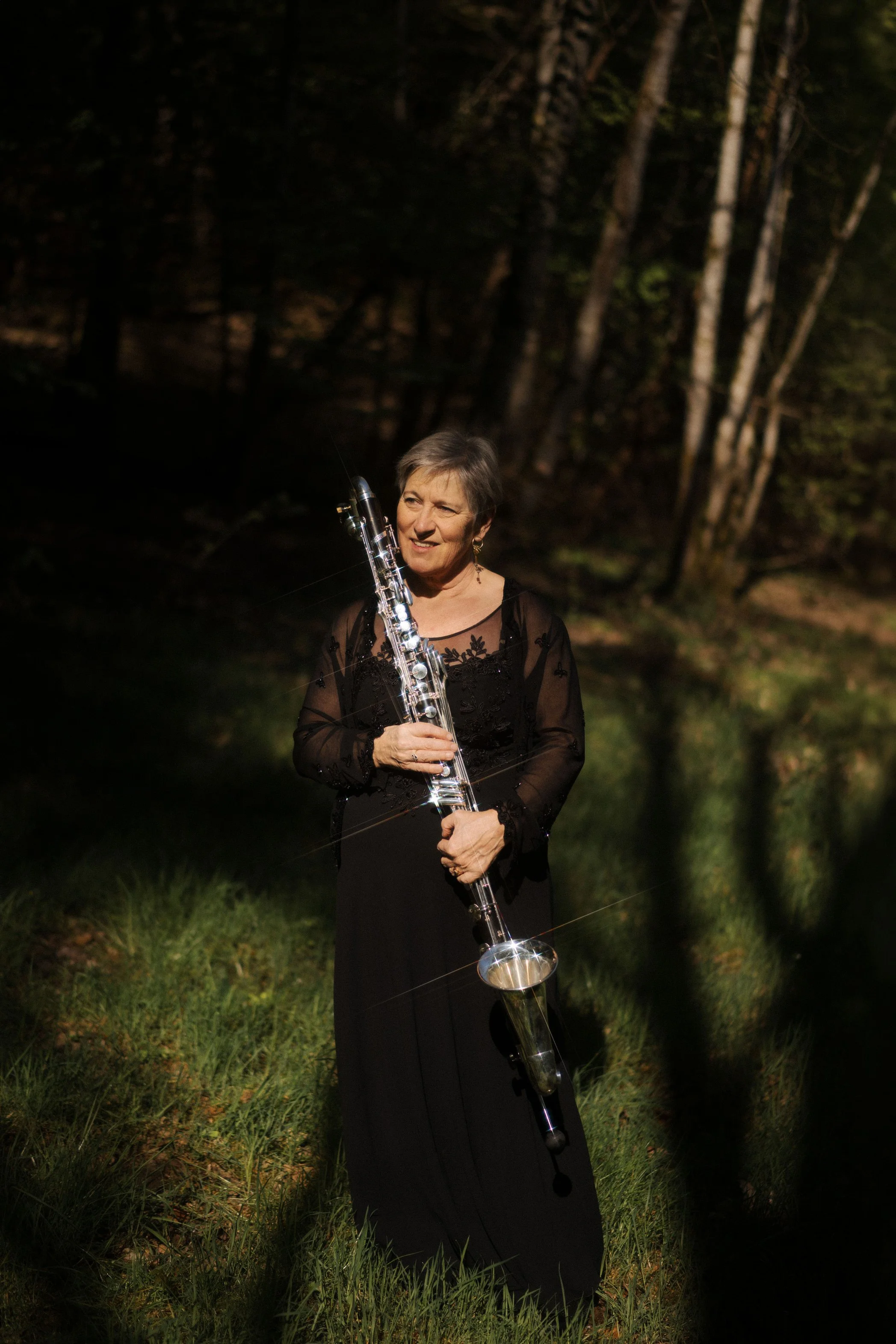 Une femme en robe noire jouant du saxophone dans une forêt la nuit.