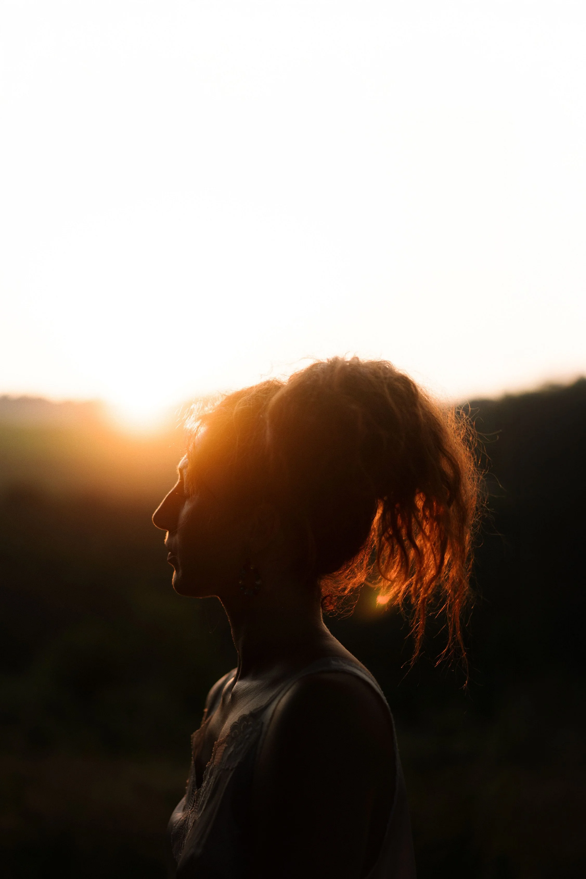 Silhouette d'une femme avec une coiffure bouclée, portant des boucles d'oreilles, au coucher du soleil en plein air.
