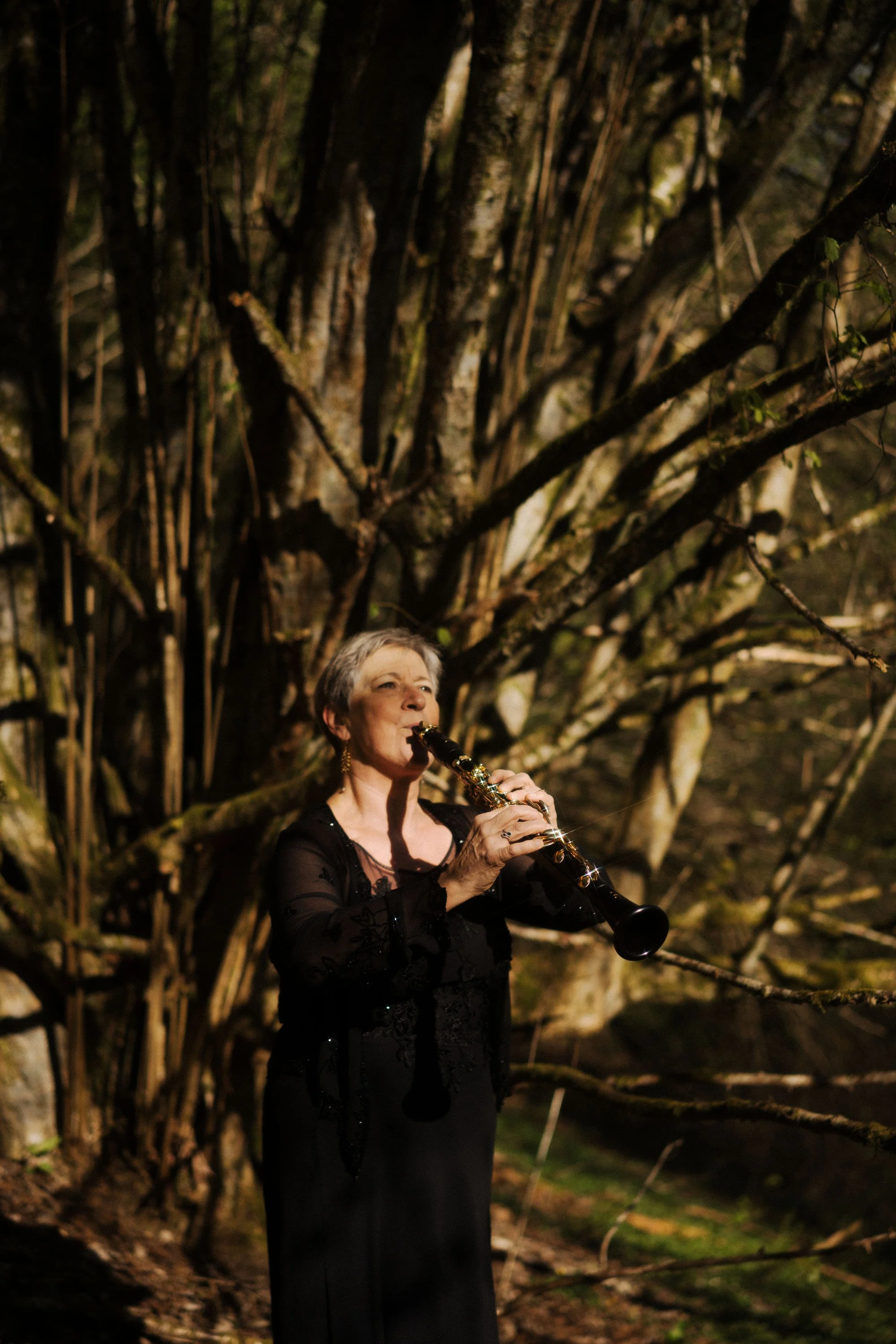 Une femme jouant du saxophone dans un environnement naturel, entourée de branches d'arbres lors d'une soirée.