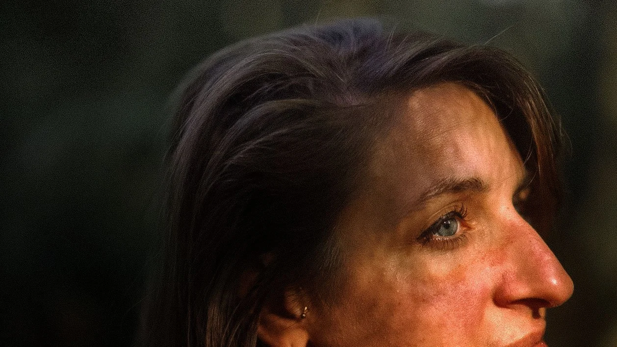 Close-up d'une femme avec des cheveux bruns, yeux bleus et peau légèrement rougie, regardant vers la droite.
