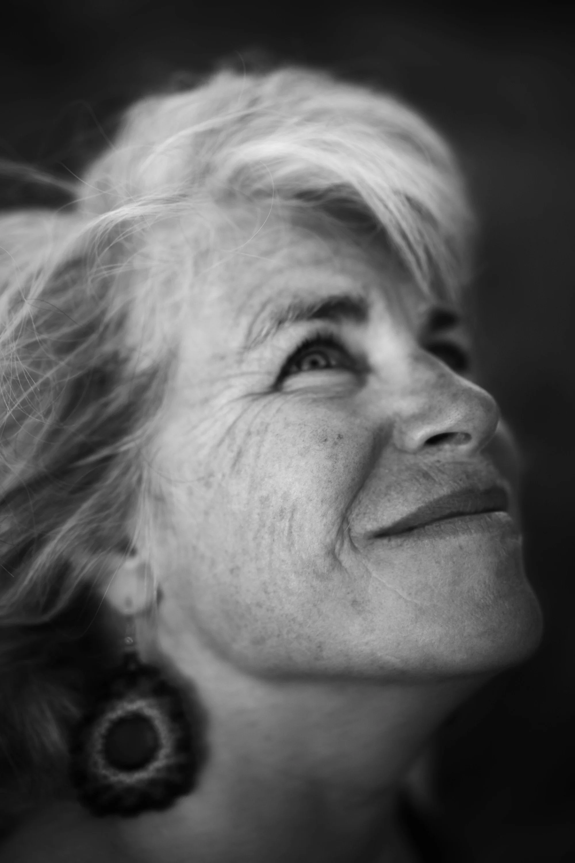Un portrait en noir et blanc d'une femme âgée avec des cheveux gris et des rides, regardant vers le haut avec une expression joyeuse.
