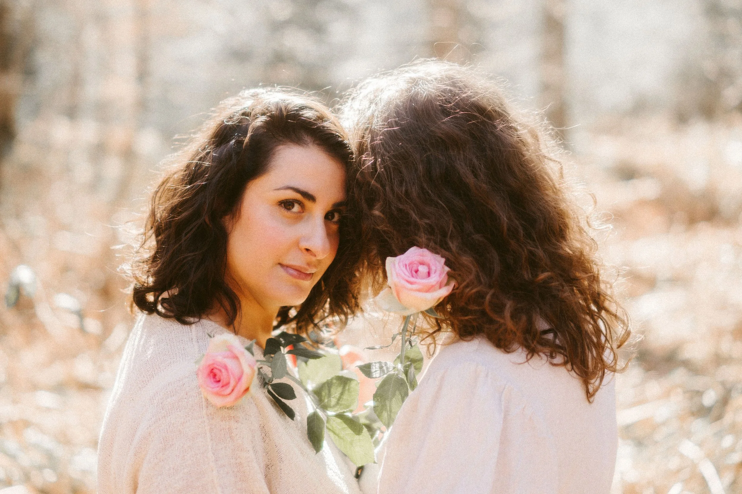 Deux femmes avec des cheveux bouclés, l'une regardant vers la caméra, tiennent des bouquets de roses.