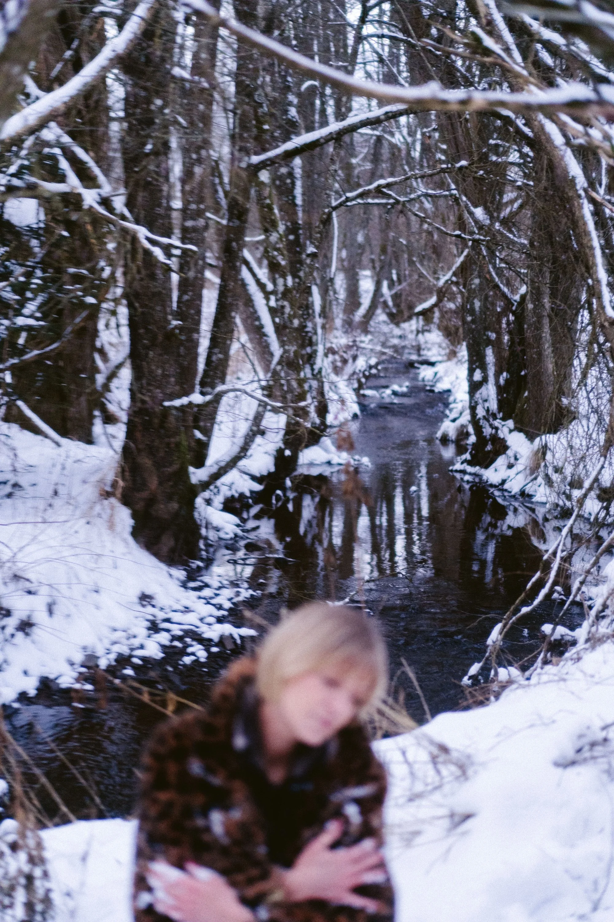 Une femme floutée près d'une rivière dans une forêt enneigée.