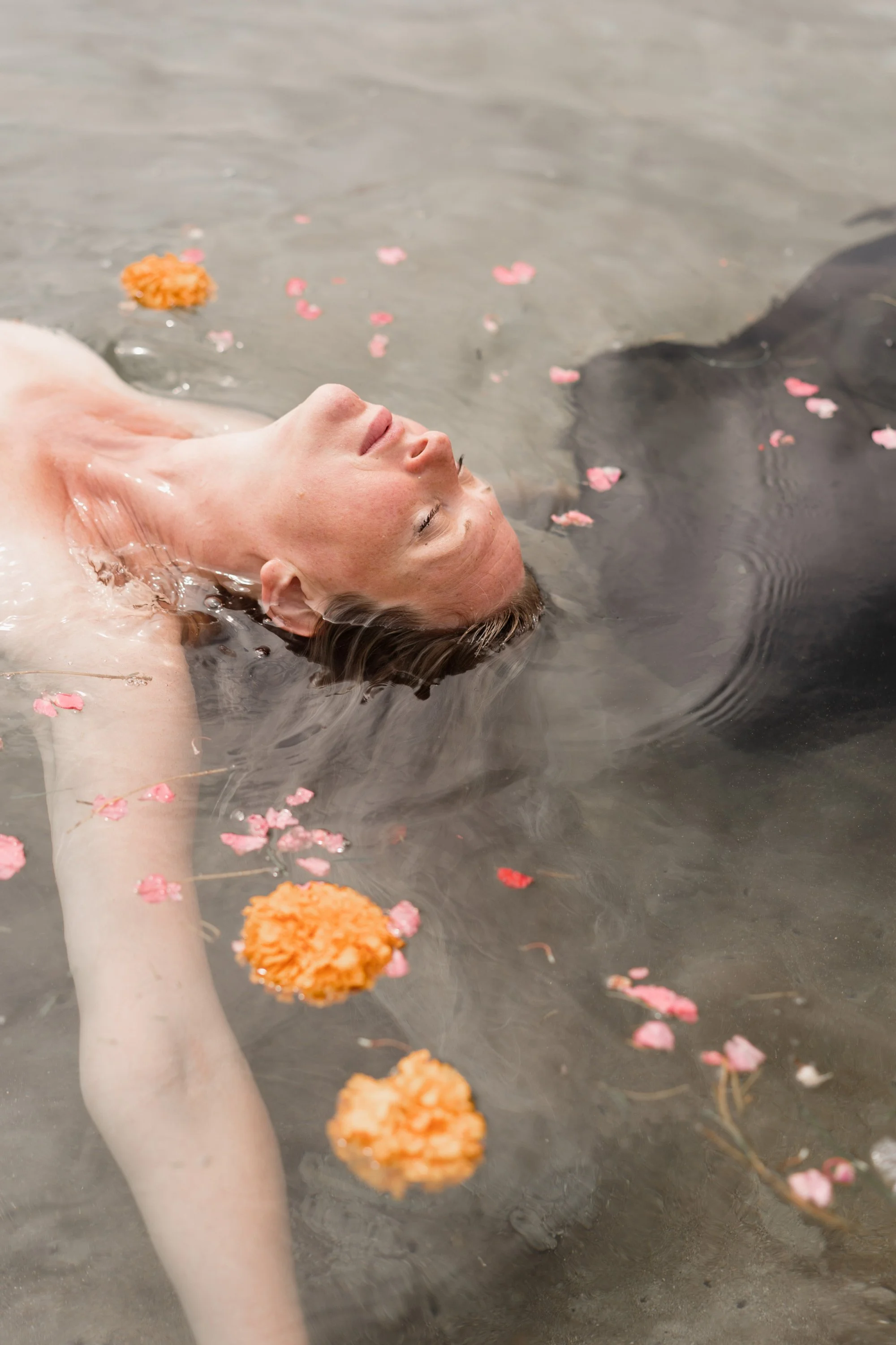 Une personne nage dans l'eau calme, entourée de fleurs de roze et une fleur orange flottant à la surface.