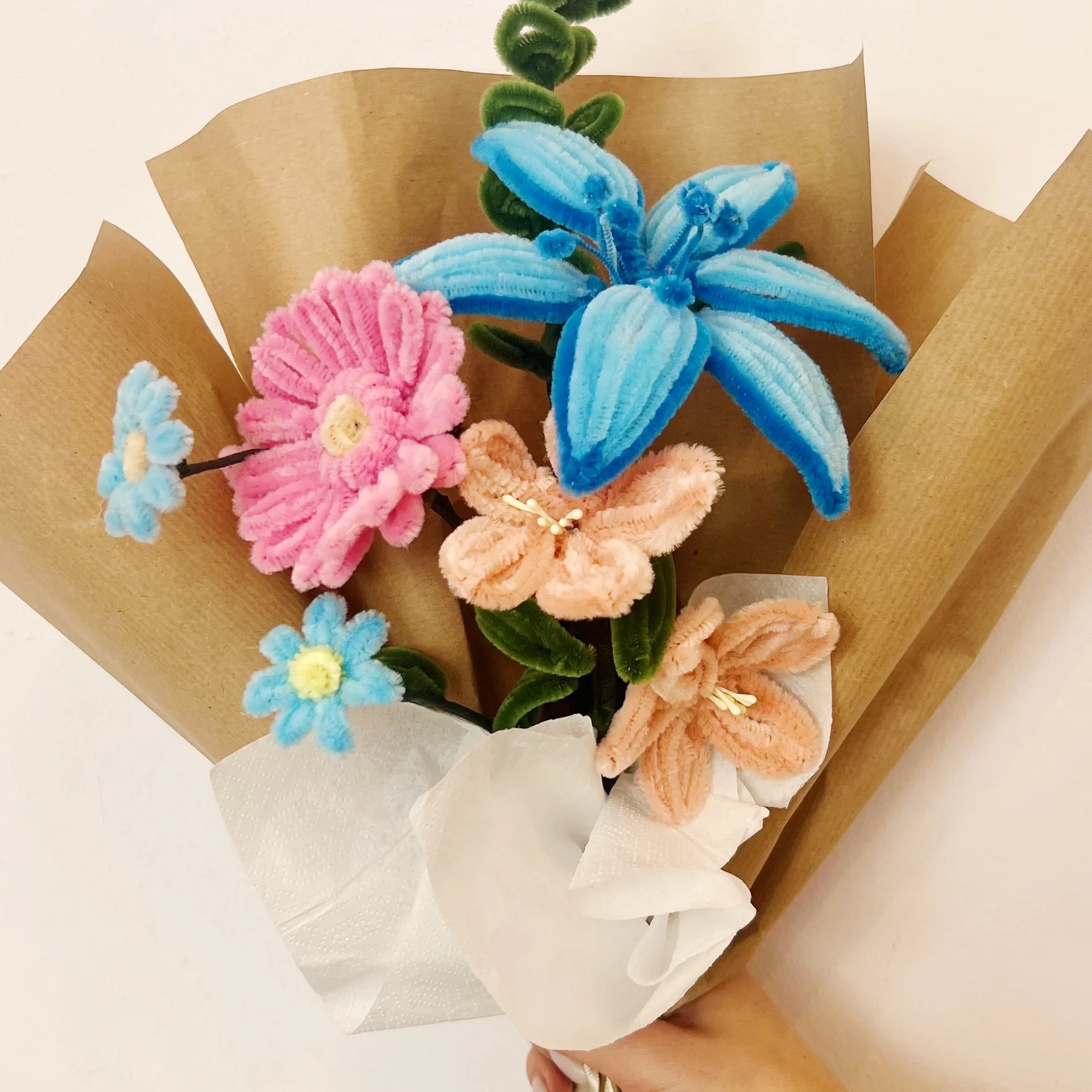 Blumenstrauß aus bunten, gestickten Blumen in rosa, blau und orange, eingehüllt in braunes und weißes Papier