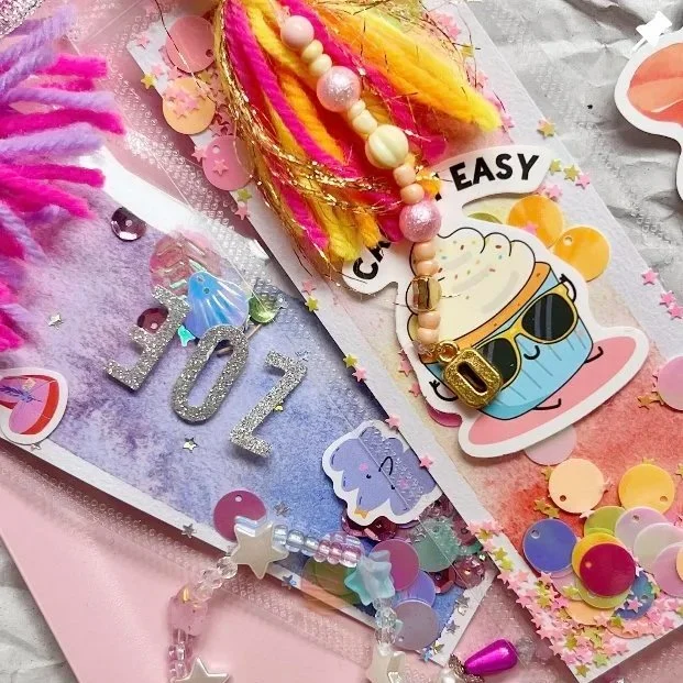 Bunte Dekoration mit Konfetti, Glitzer, einer Zahl 2023, einer Pappfigur mit Ananas und Sonnenbrille, bunten Federn, Perlenkette mit Buchstabe D, und Party-Accessoires.