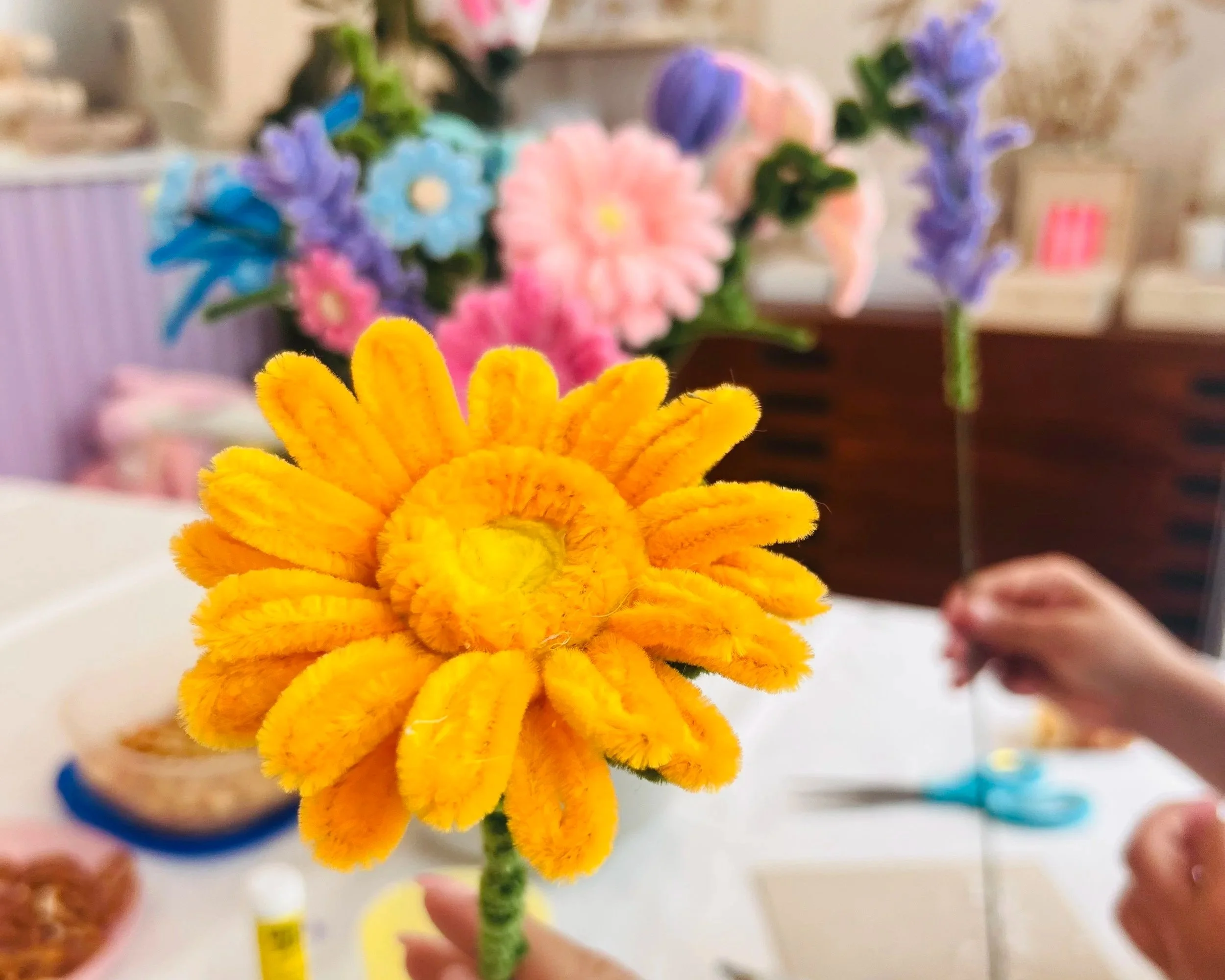 Bunte künstliche Blumen in Gelb, Pink, Blau und Lila, gehalten in einer Hand in der Nähe.