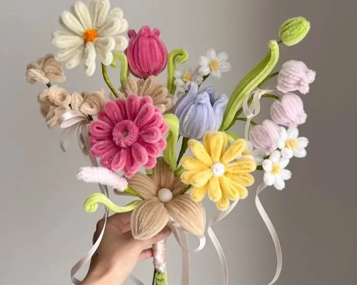 Hand hält einen bunten Strauß aus gestrickten und gehäkelten Stoffblumen in verschiedenen Farben