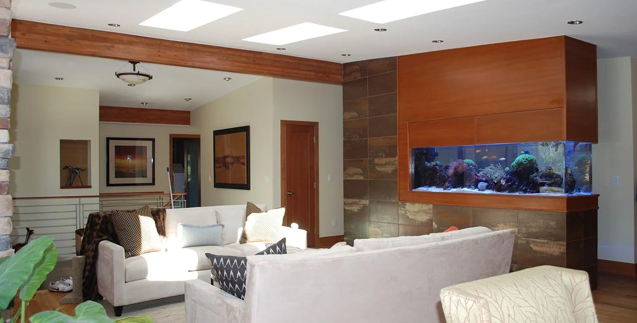 Living room with beige sofas, decorative throw pillows, a built-in aquarium, and wooden accents on the ceiling and walls.