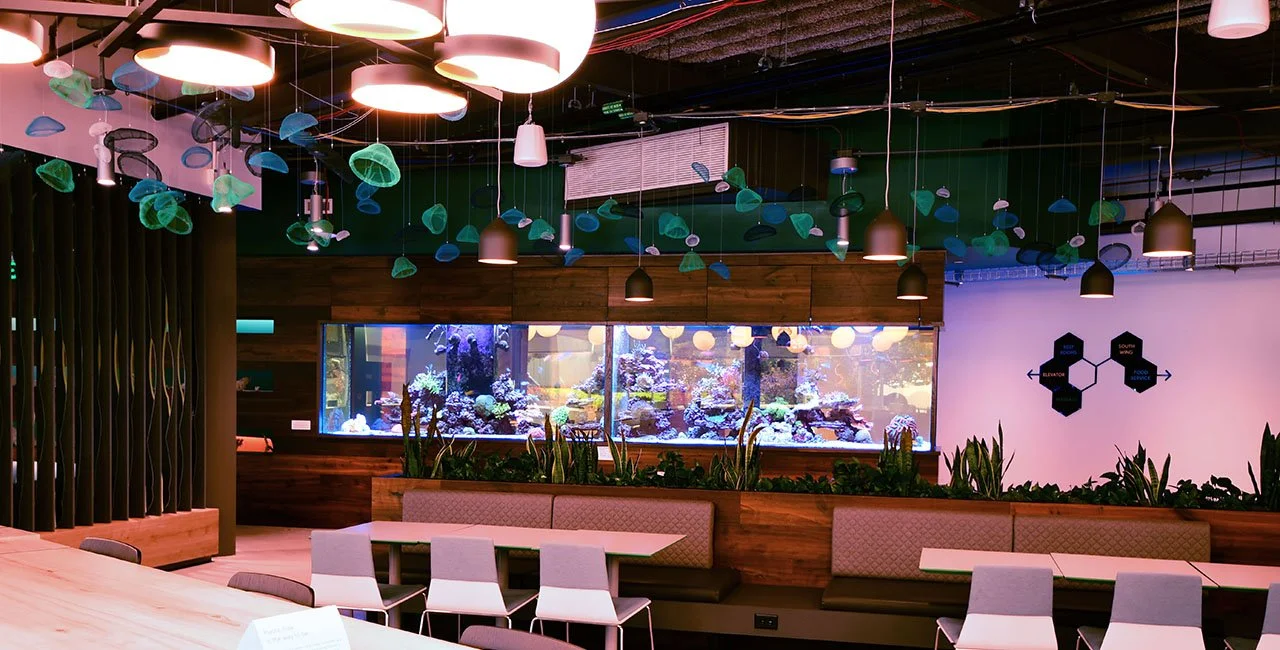 An interior room with hanging lights, an aquarium with coral and fish, and seating areas with tables and chairs.