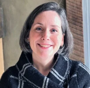 Headshot of smiling female with short, black-gray hair in a black and gray plaid sweater.