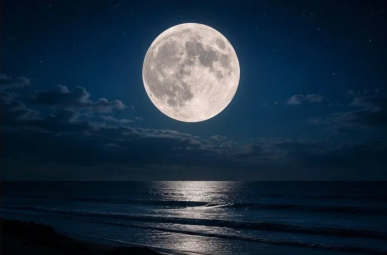 Full moon over the ocean at night with reflections on the water and some clouds in the sky.