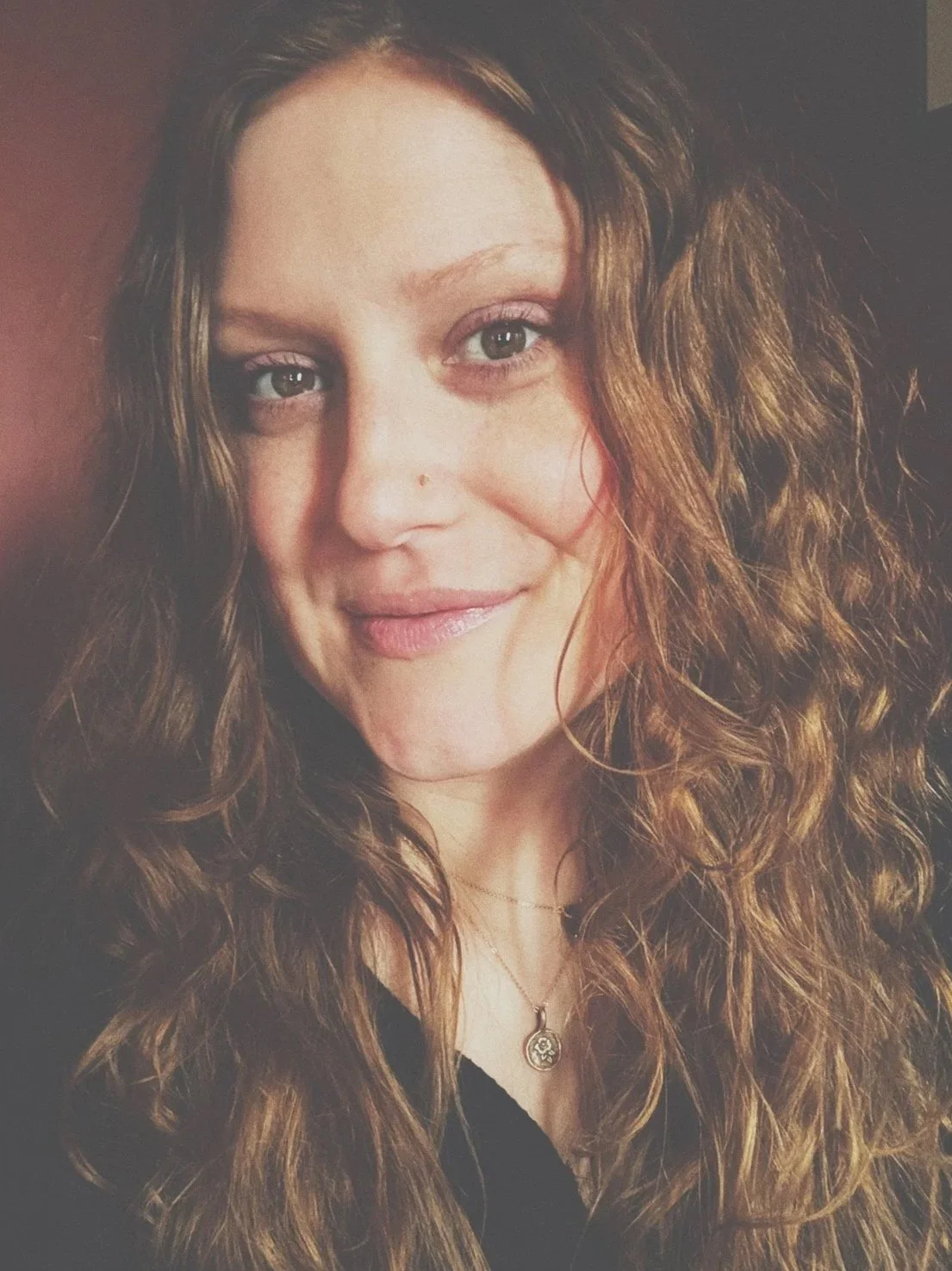 Close-up of a woman with long curly hair wearing a necklace with a pendant.