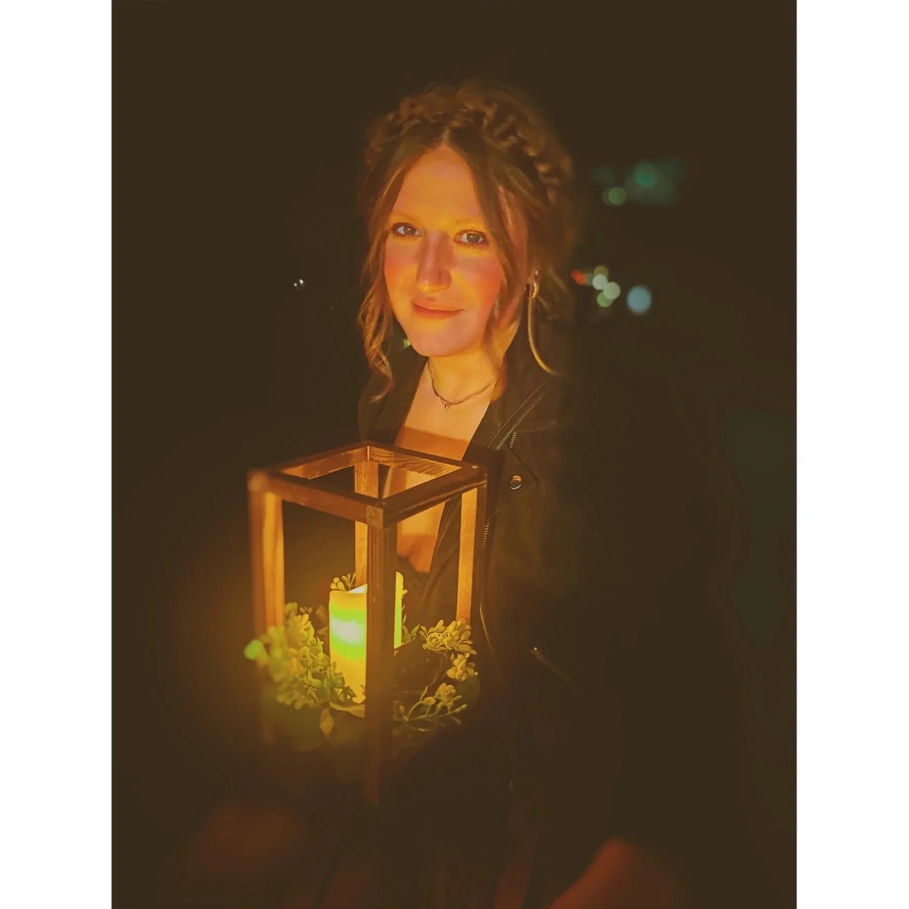 A woman with long hair and earrings lighting a lantern during nighttime, surrounded by flowers.