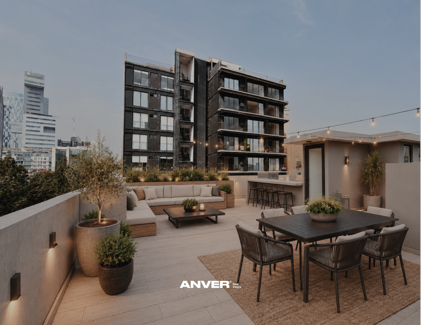Terraza en un edificio de apartamentos con sillones, mesa y plantas decorativas, vista a la ciudad con edificios altos.