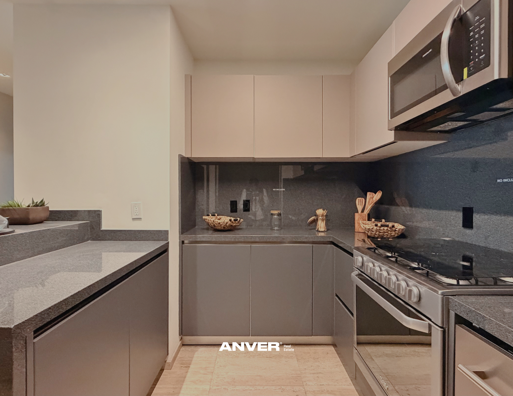 Cocina moderna con gabinetes claros, encimera de granito, microondas y estufa de gas, decorada con cestas y utensilios de cocina en la encimera.