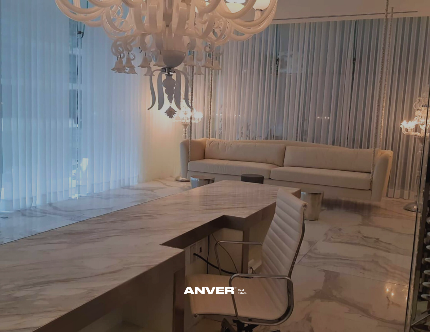 Sala de estar elegante con sofá beige, cortinas de cristal, mesas laterales, candelabros y un comedor de mármol.