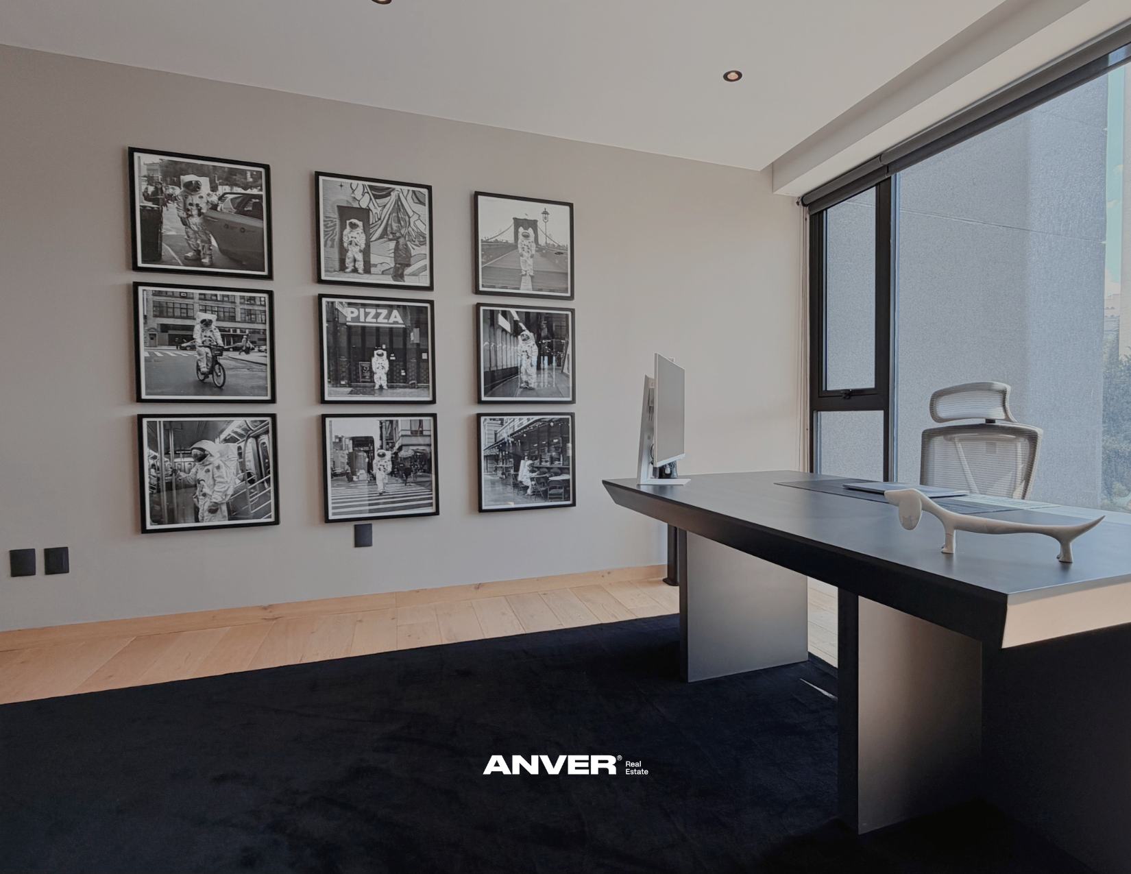 Sala de oficina moderna con pared decorada con fotos en blanco y negro y un escritorio con una silla ergonómica frente a una gran ventana con vista a la ciudad.