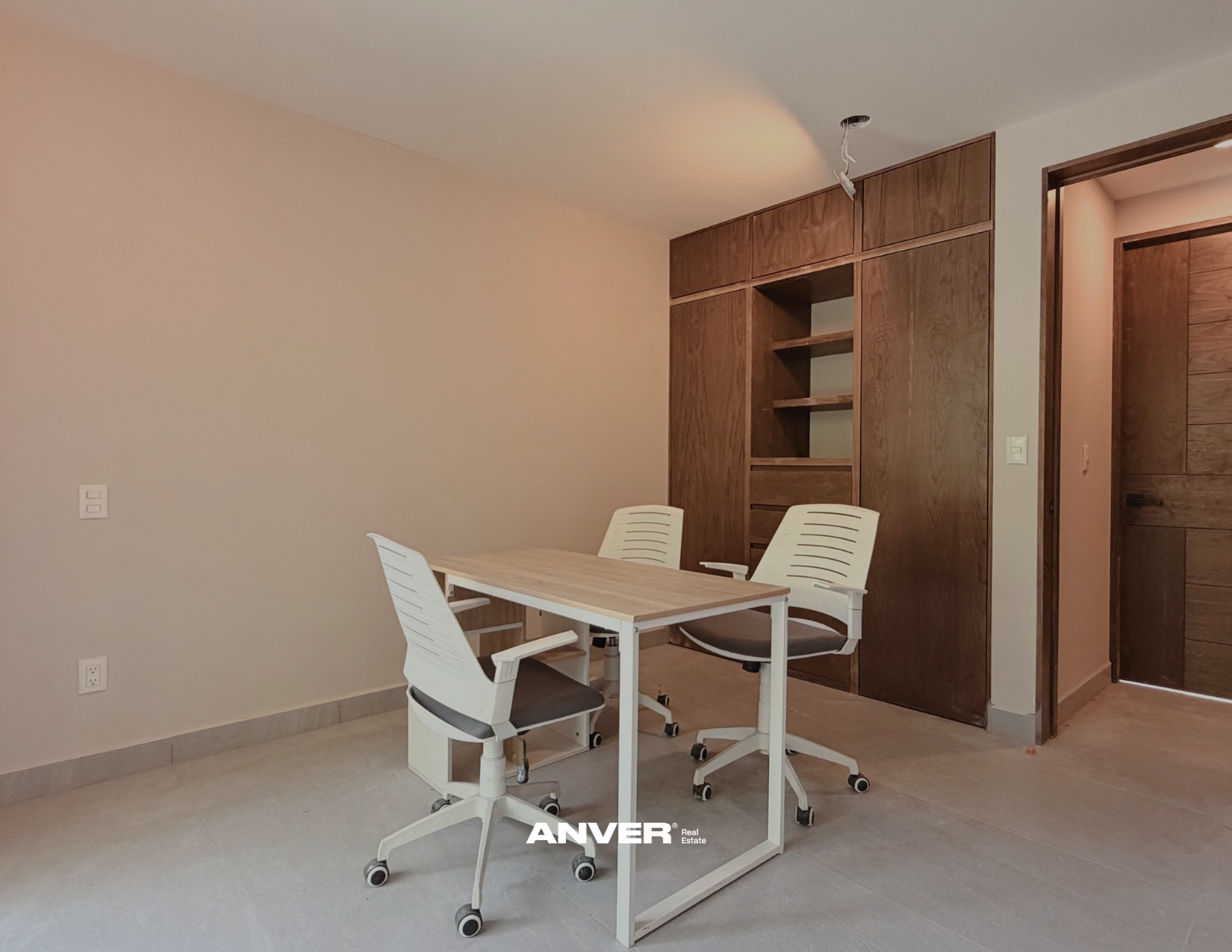 Sala de juntas con mesa y sillas blancas, paredes blancas, armario de madera y puerta de madera, suelo de baldosas, luz natural