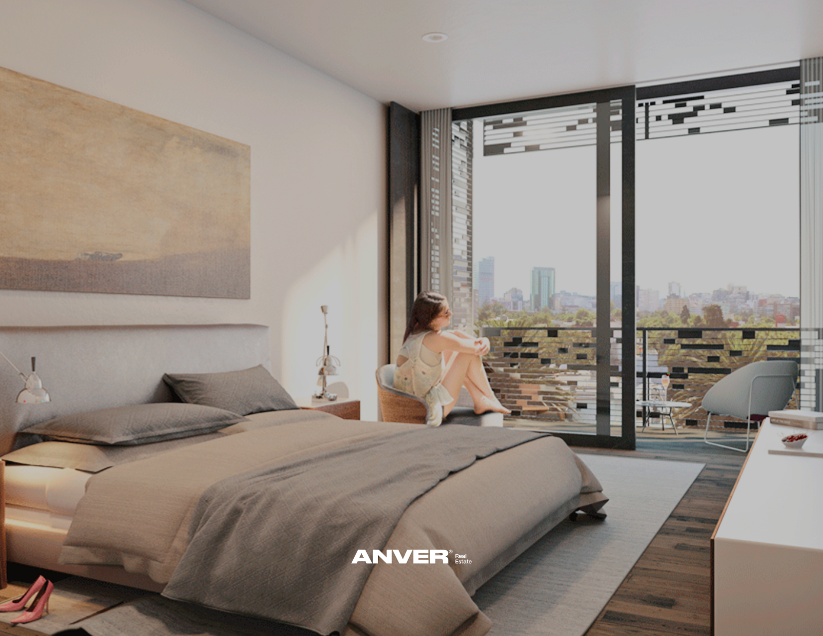 Habitación moderna con cama doble en primer plano y una mujer sentada en un sillón mirando por la ventana. Ventana grande con vista a la ciudad y balcón con mobiliario.