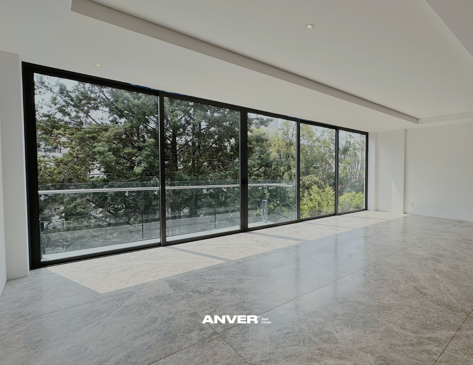 Sala vacía con grandes ventanas de vidrio que muestran árboles verdes afuera.