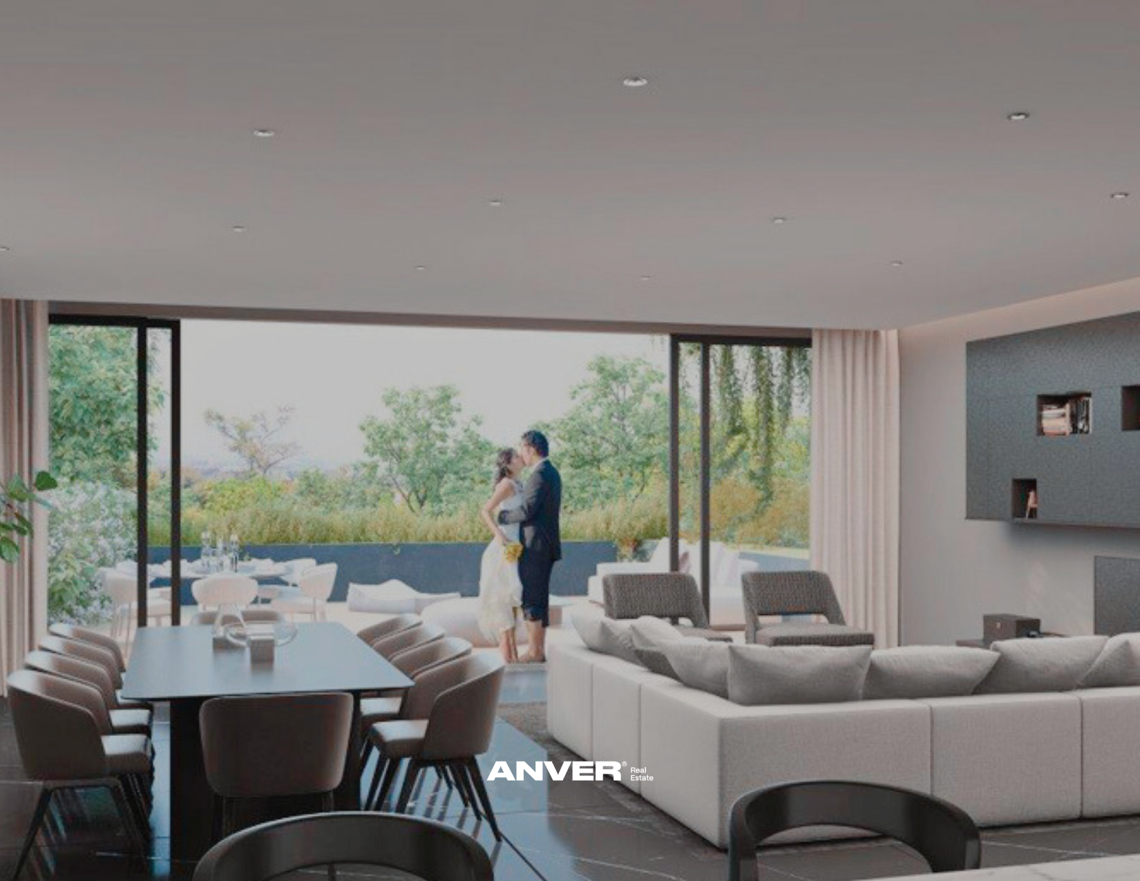 Interior moderno con pareja abrazándose junto a grandes ventanales con vista a árboles y naturaleza, sala de estar con sillones y comedor de madera y sillas modernas.