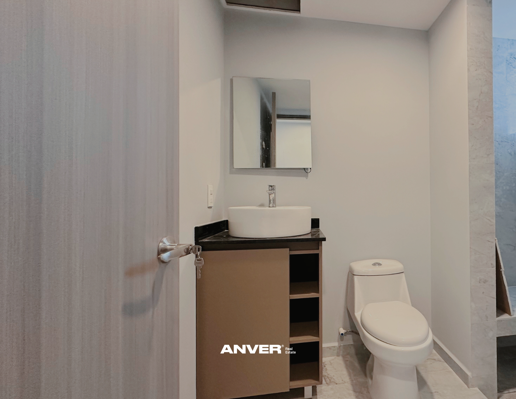 Baño moderno con lavabo de cerámica sobre mueble oscuro, espejo rectangular, inodoro blanco y pared de azulejos beige y azul.