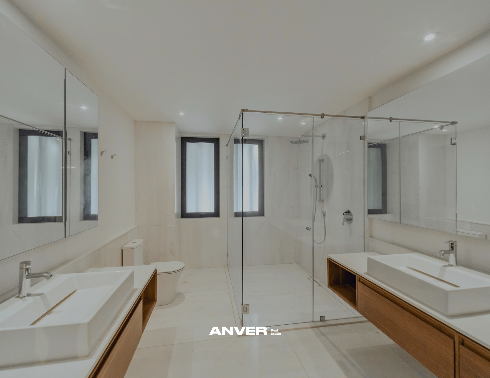 Baño moderno con doble lavabo, espejos grandes, ducha con mampara de vidrio, ventanas altas y bancas de madera