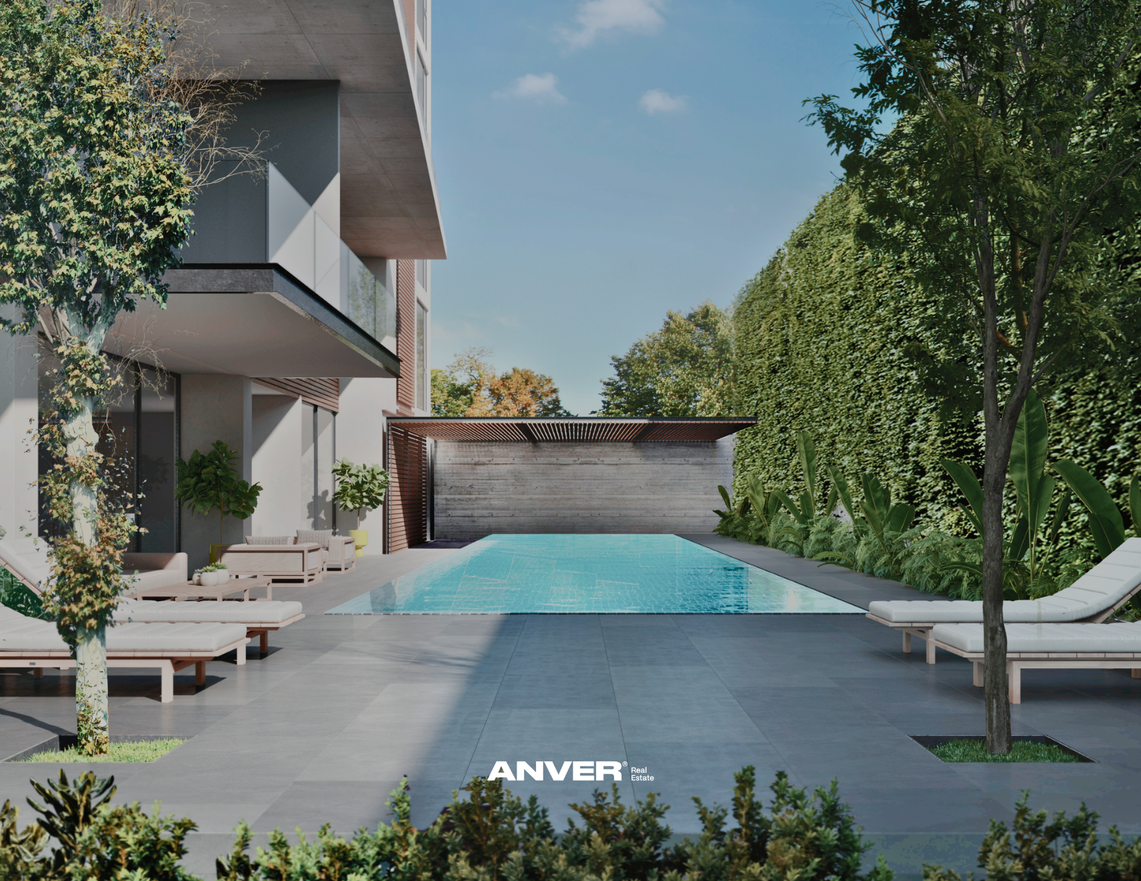 Piscina moderna en el patio trasero de una casa, rodeada de sillas largas y plantas, con paredes de cemento y un muro de madera, cielo despejado y árboles verdes