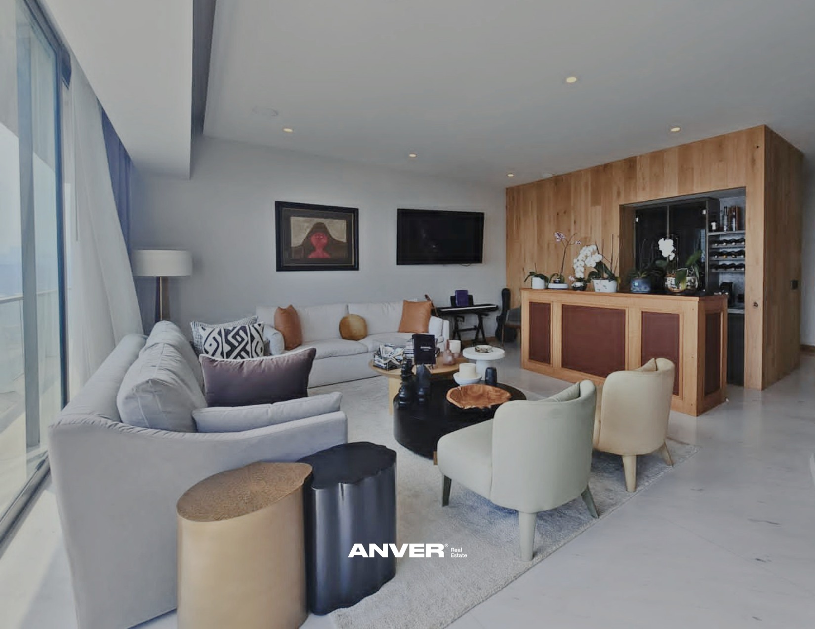 Sala de estar moderna con sillones blancos, mesa de café con objetos decorativos, paredes blancas con cuadros y televisión, bar de madera con plantas y vino