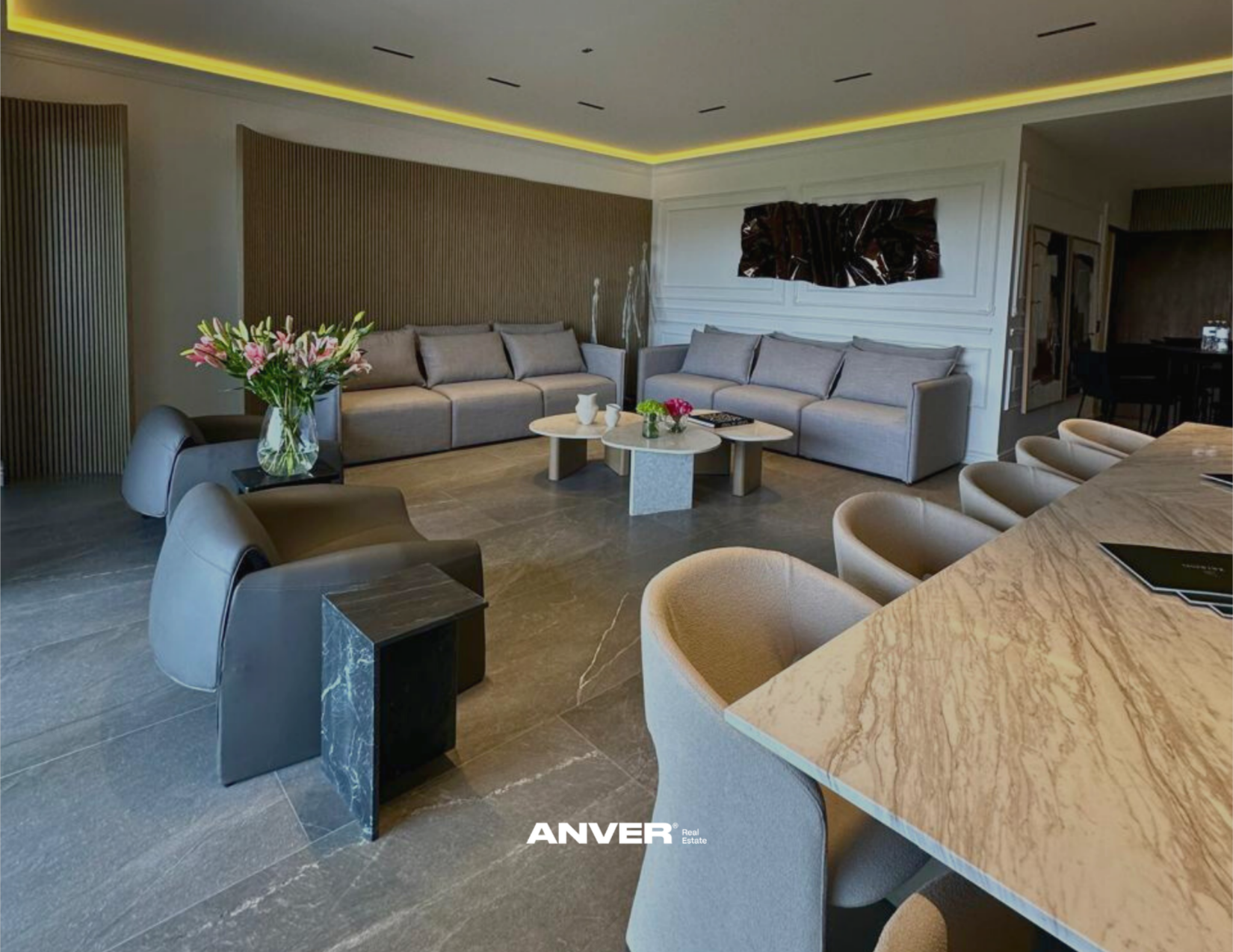 Sala de estar moderna con sillones grises, mesa de centro de piedra con flores y jarrones, y una pared decorativa de madera