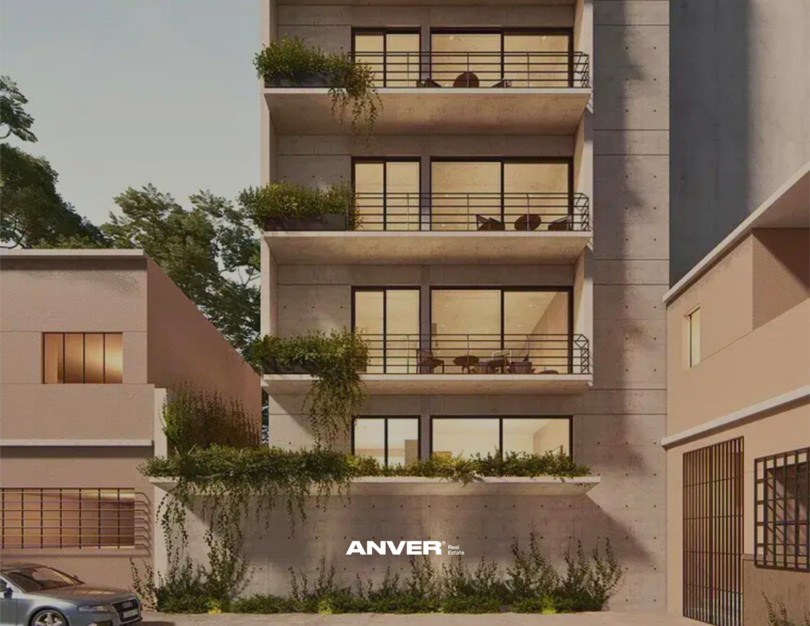 Edificio moderno de varios pisos con balcones con plantas y muebles en la fachada, durante la noche, con autos estacionados abajo.