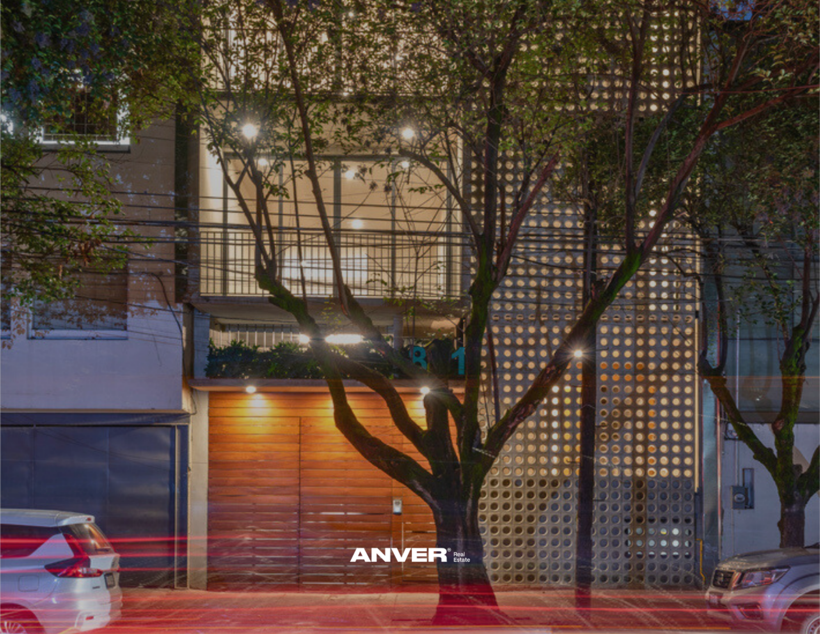 Edificio con ventana, reja, árbol en la calle, y autos estacionados, iluminado en la noche