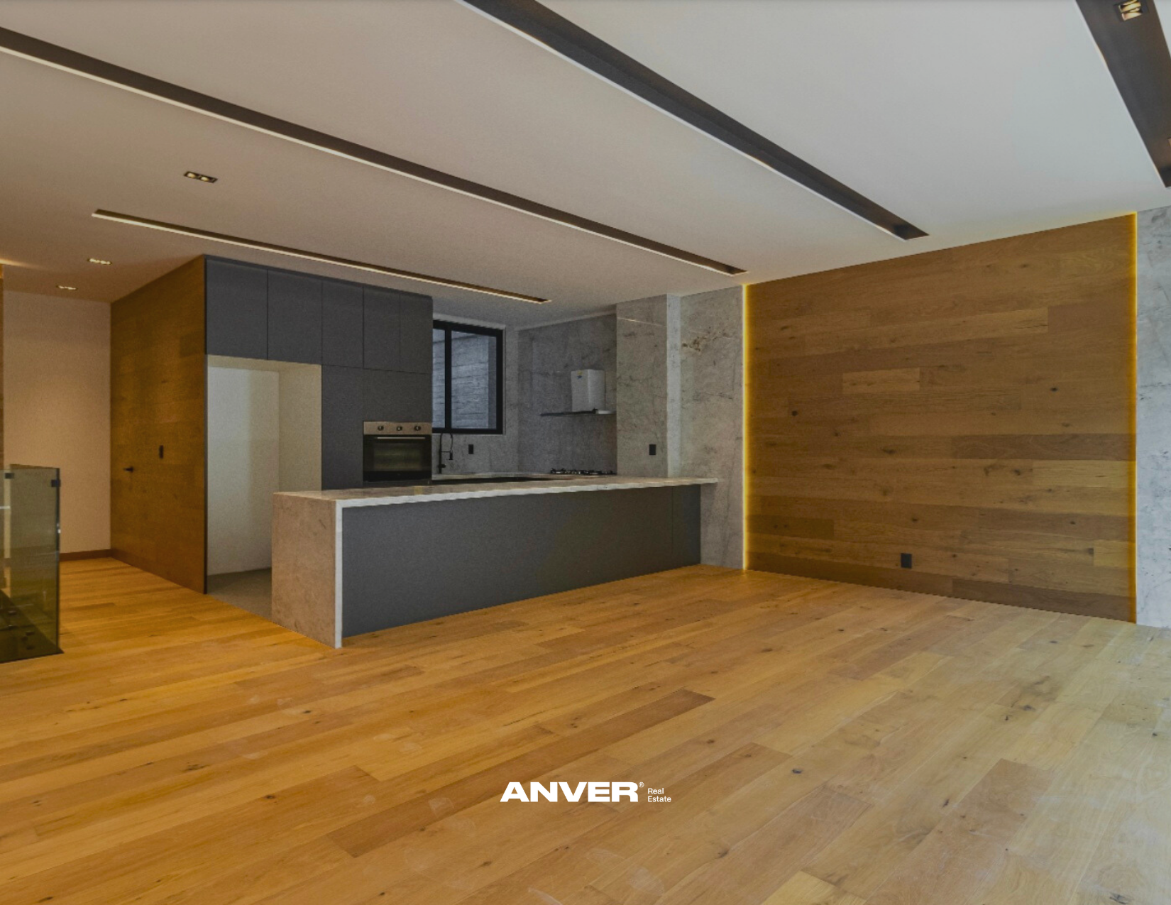 Espacio de cocina y sala con paredes de madera y paredes de piedra, con encimera de mármol y armarios oscuros, suelo de madera, techo suspendido con luces empotradas y ventana en la pared trasera.
