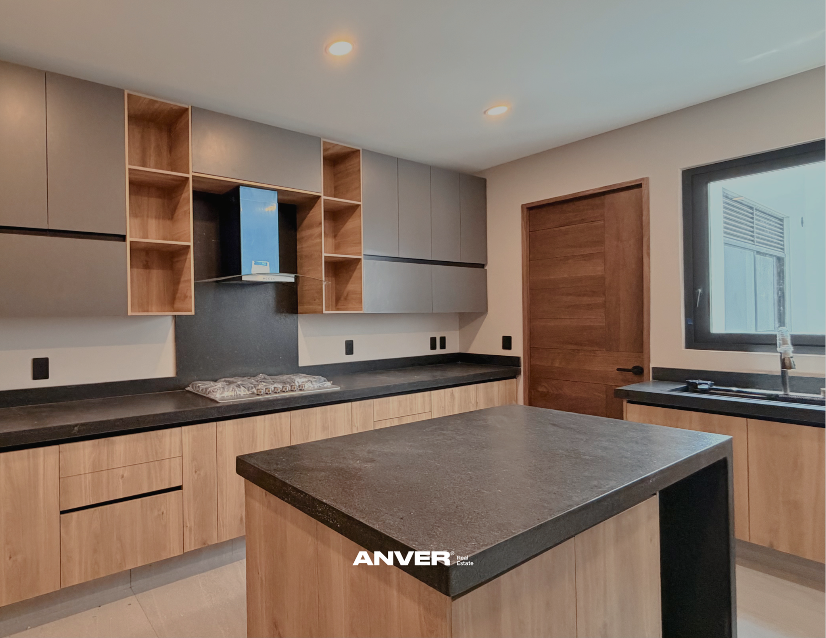 Cocina moderna con gabinetes de madera y encimera de piedra, ventana y puerta de madera.