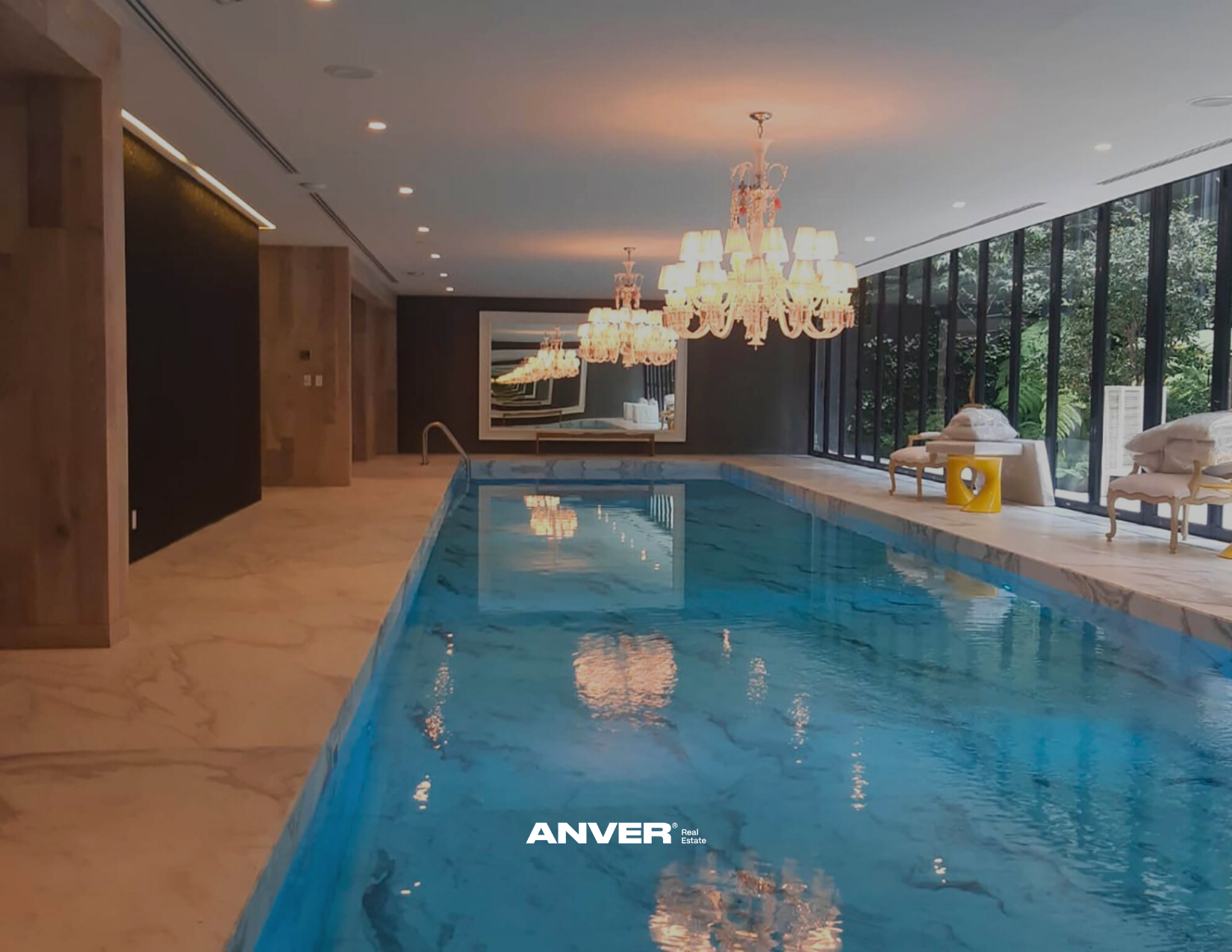 Interior de una piscina cubierta con candelabros y grandes ventanales con vista a jardines.