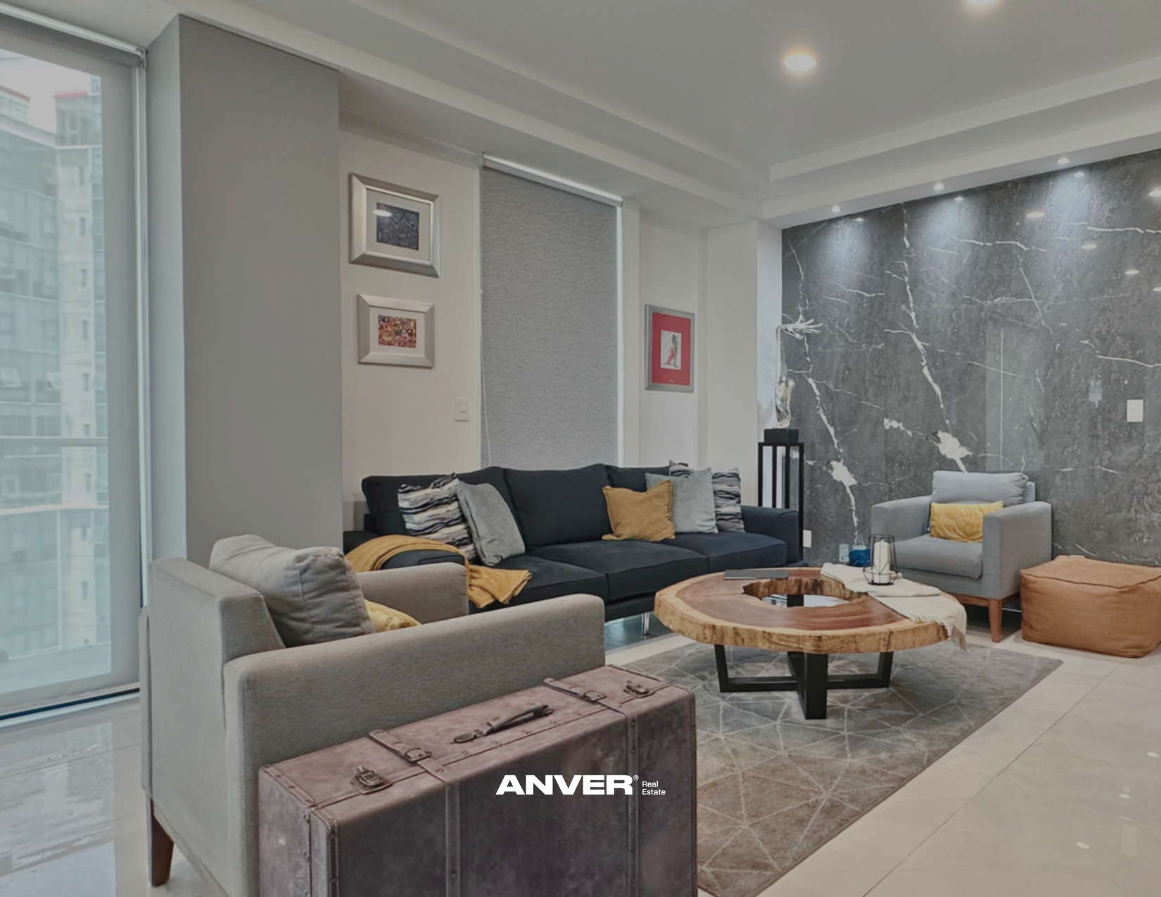 Sala moderna con sillón gris, sofá negro con cojines y sillón gris con cojines amarillos, mesa de madera y decoración en paredes de mármol oscuro.